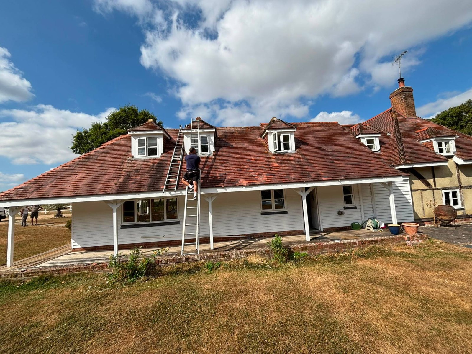 Roofer on a ladder at a white weatherboarded house with dormer windows