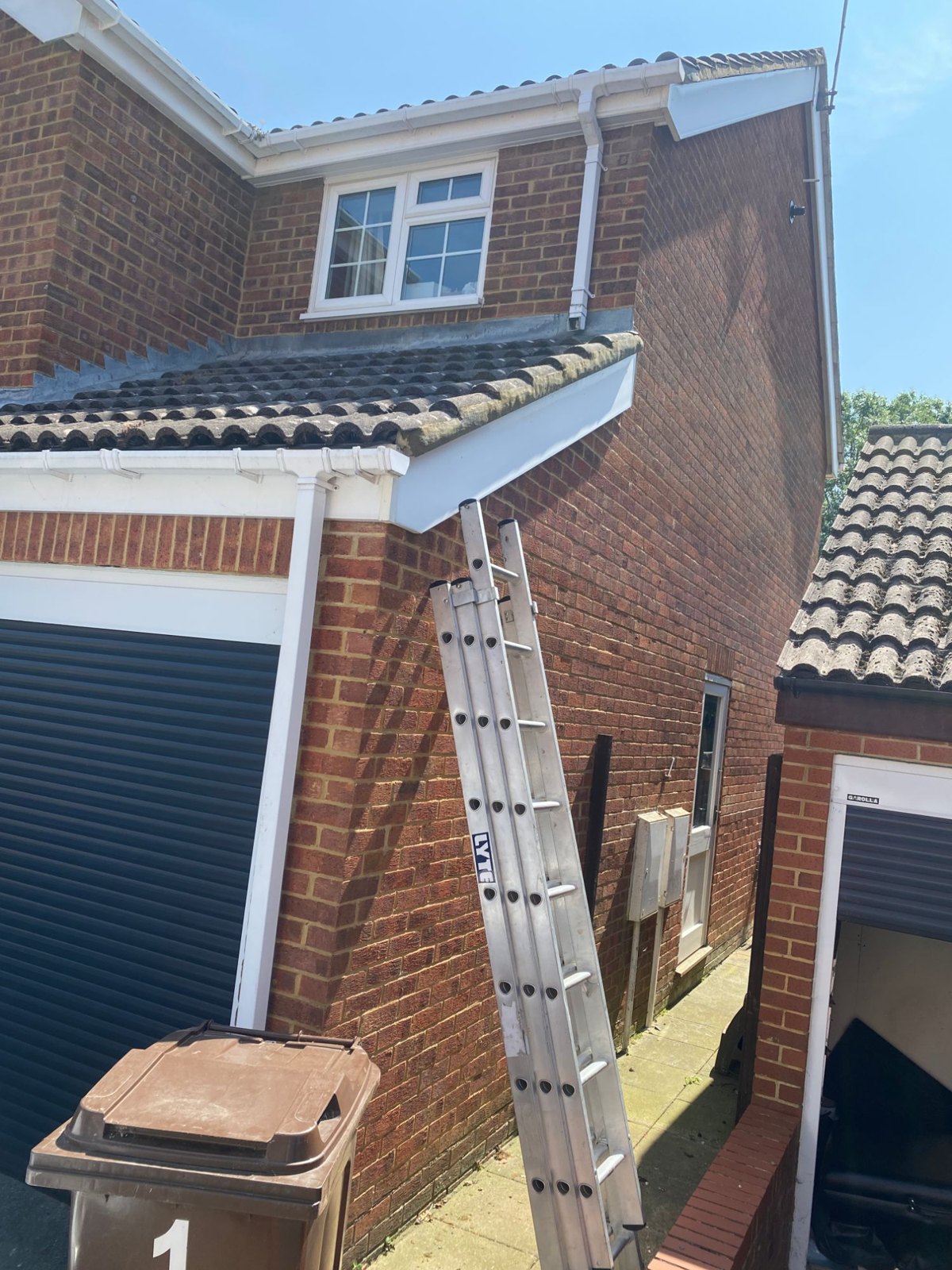 Ladder against the roofline of a brick house with white fascias and guttering