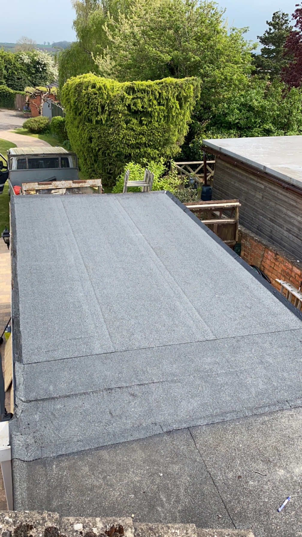 Grey mineral felt flat roof laid over an extension, with a garden and hedge beyond