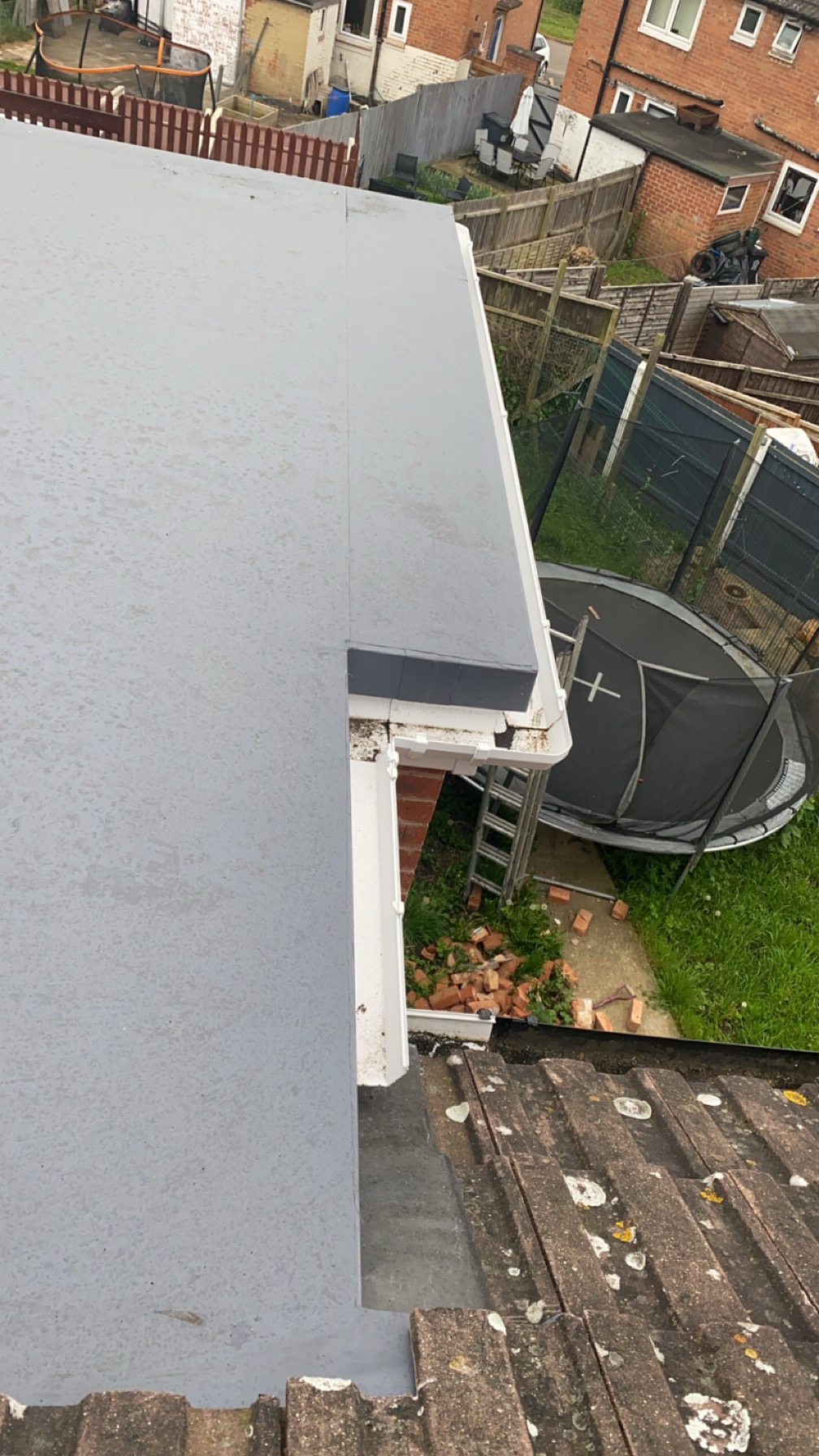 Edge detail of a grey flat roof meeting new white fascia and guttering above a tiled pitched roof