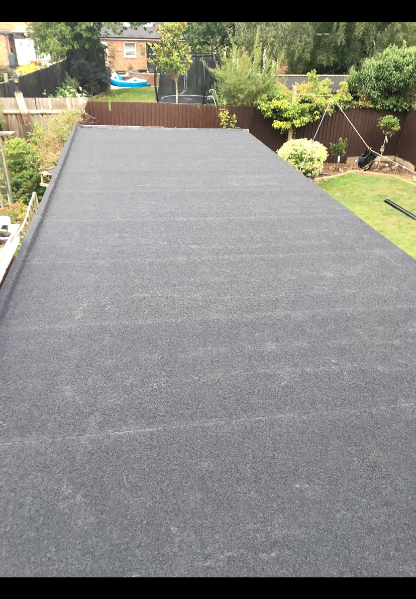 Long dark grey felt flat roof over a garden room, with a lawn and fencing behind