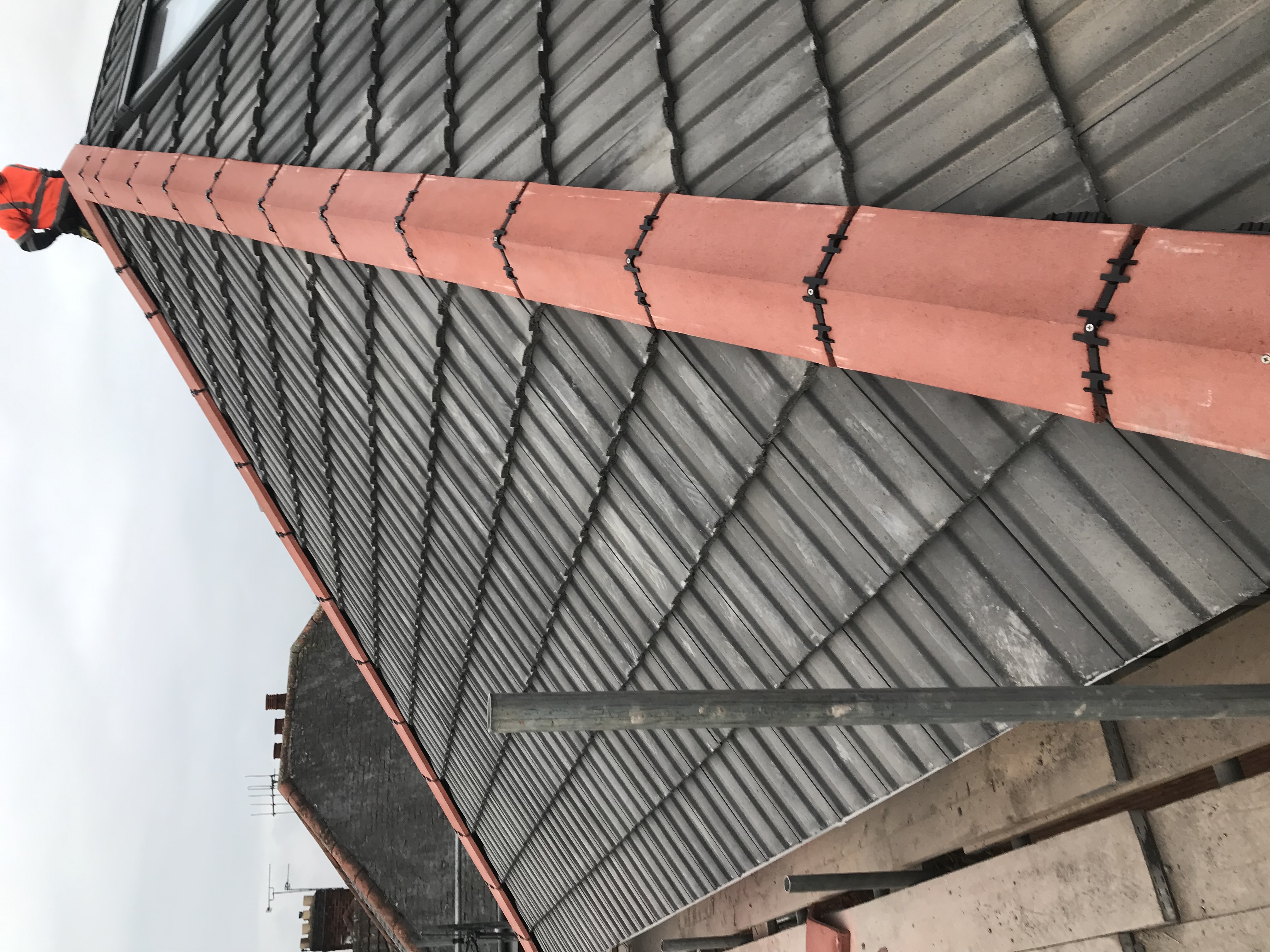 Grey concrete tiled roof with a red clay ridge and hip tiles being fitted from scaffolding