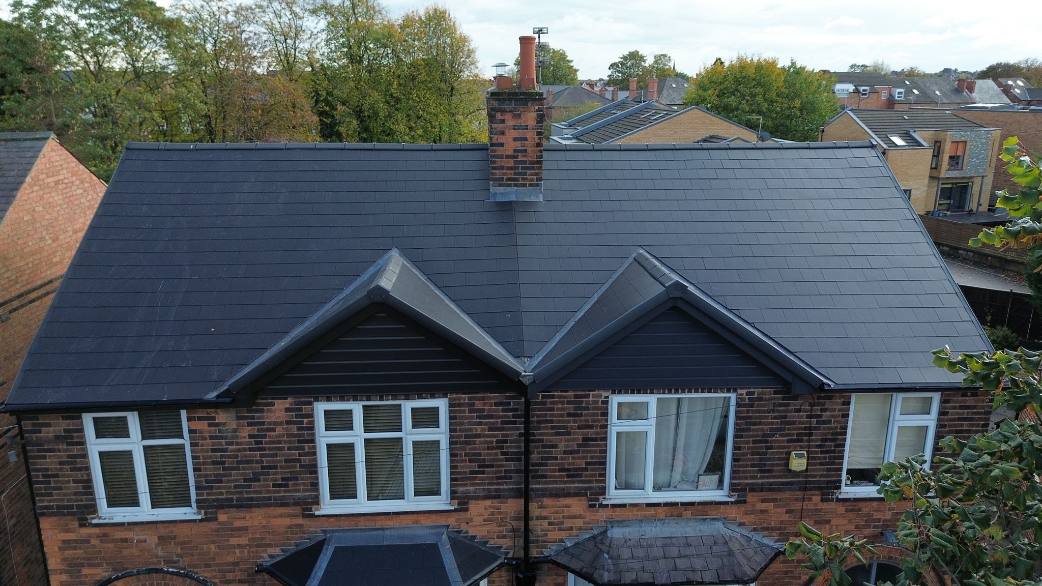 Aerial view of a finished dark grey slate roof on a red brick semi-detached house with twin gables and a brick chimney