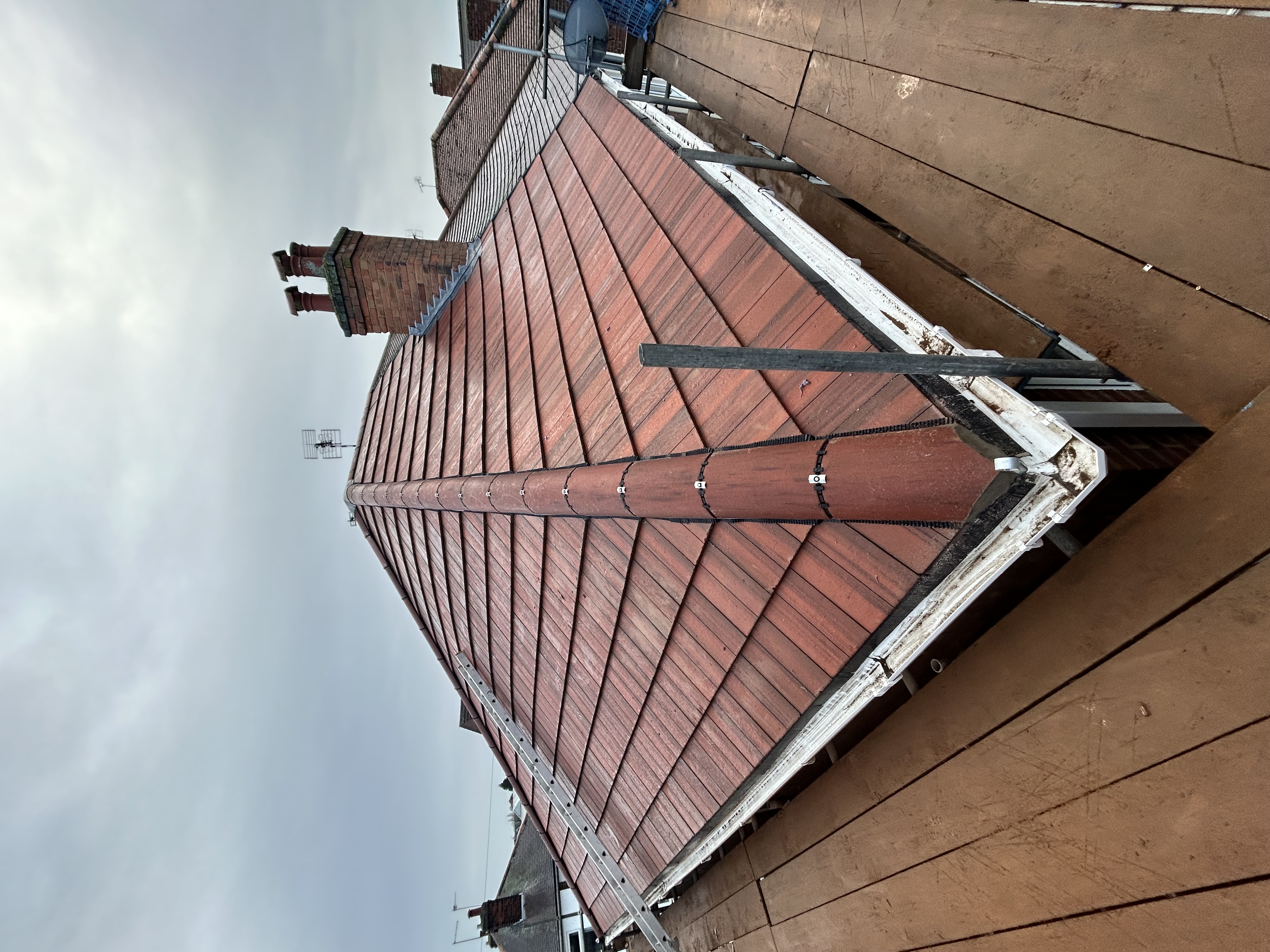 Hipped roof covered in red clay tiles with a brick chimney stack and lead flashing