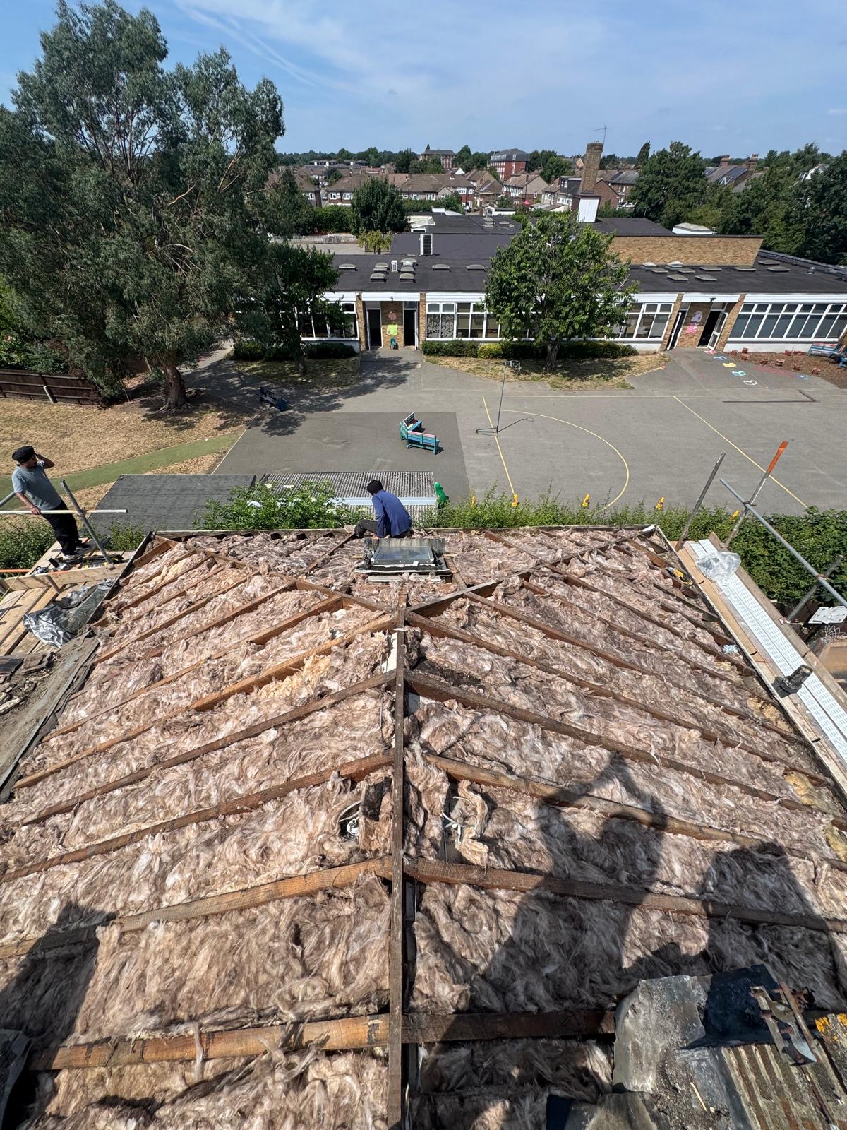A pitched house roof seen from scaffolding with newly laid grey tiles running up to the ridge