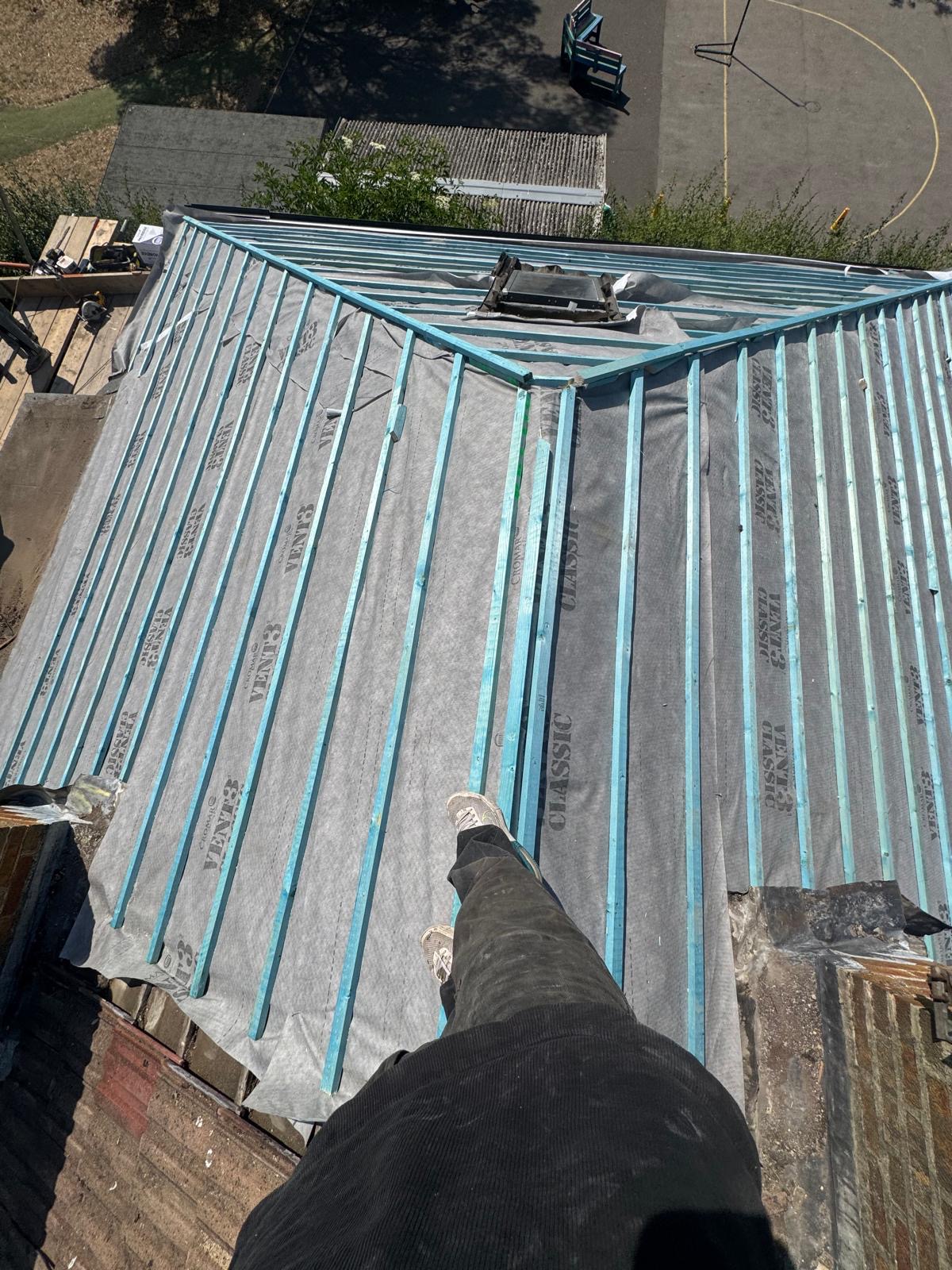 Roof slope covered in fresh grey tiles with a brick chimney stack behind
