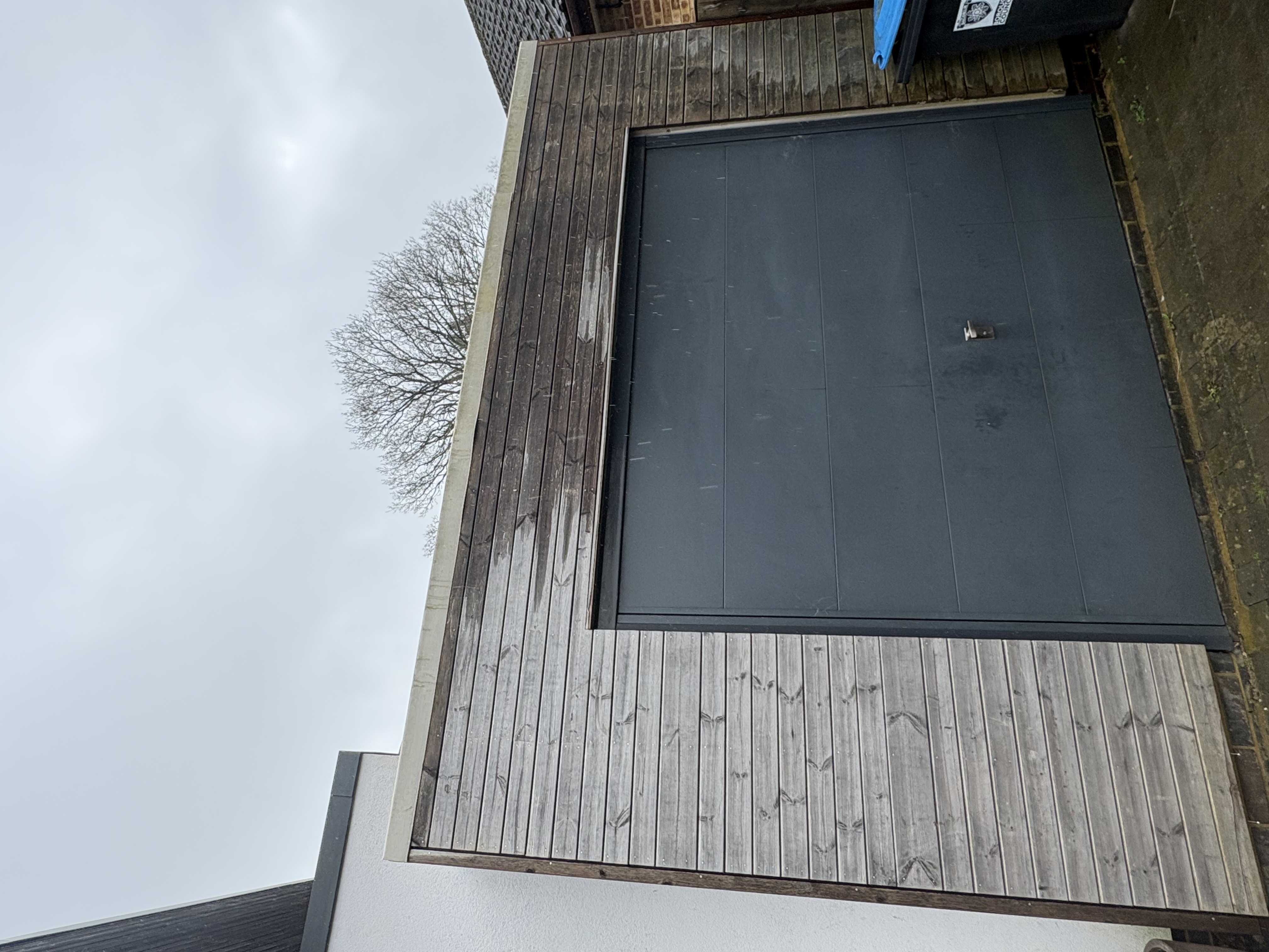 A garage with grey timber cladding, a dark grey up-and-over door and a flat roof edged with white trim