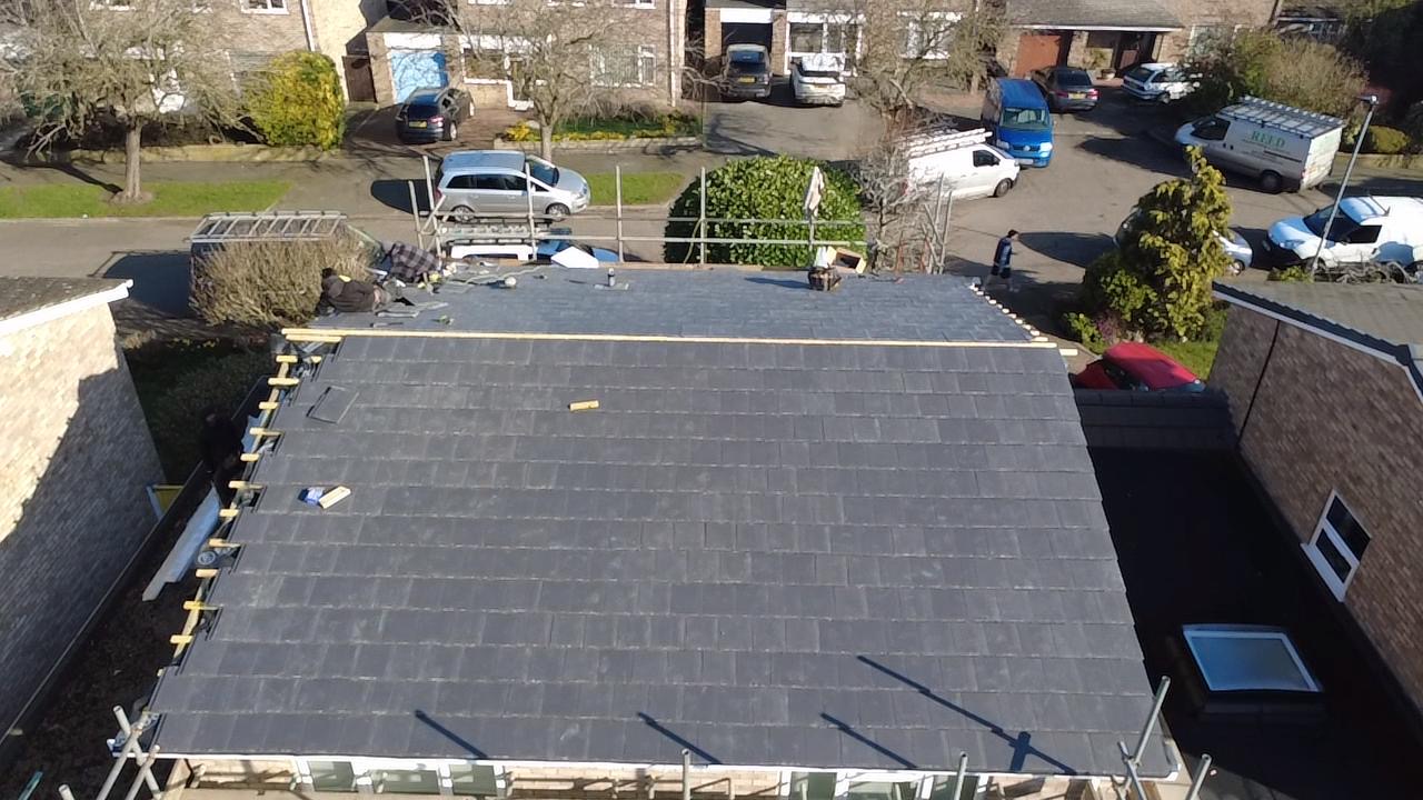 Aerial view of a freshly tiled dark grey roof with scaffolding still up along the eaves