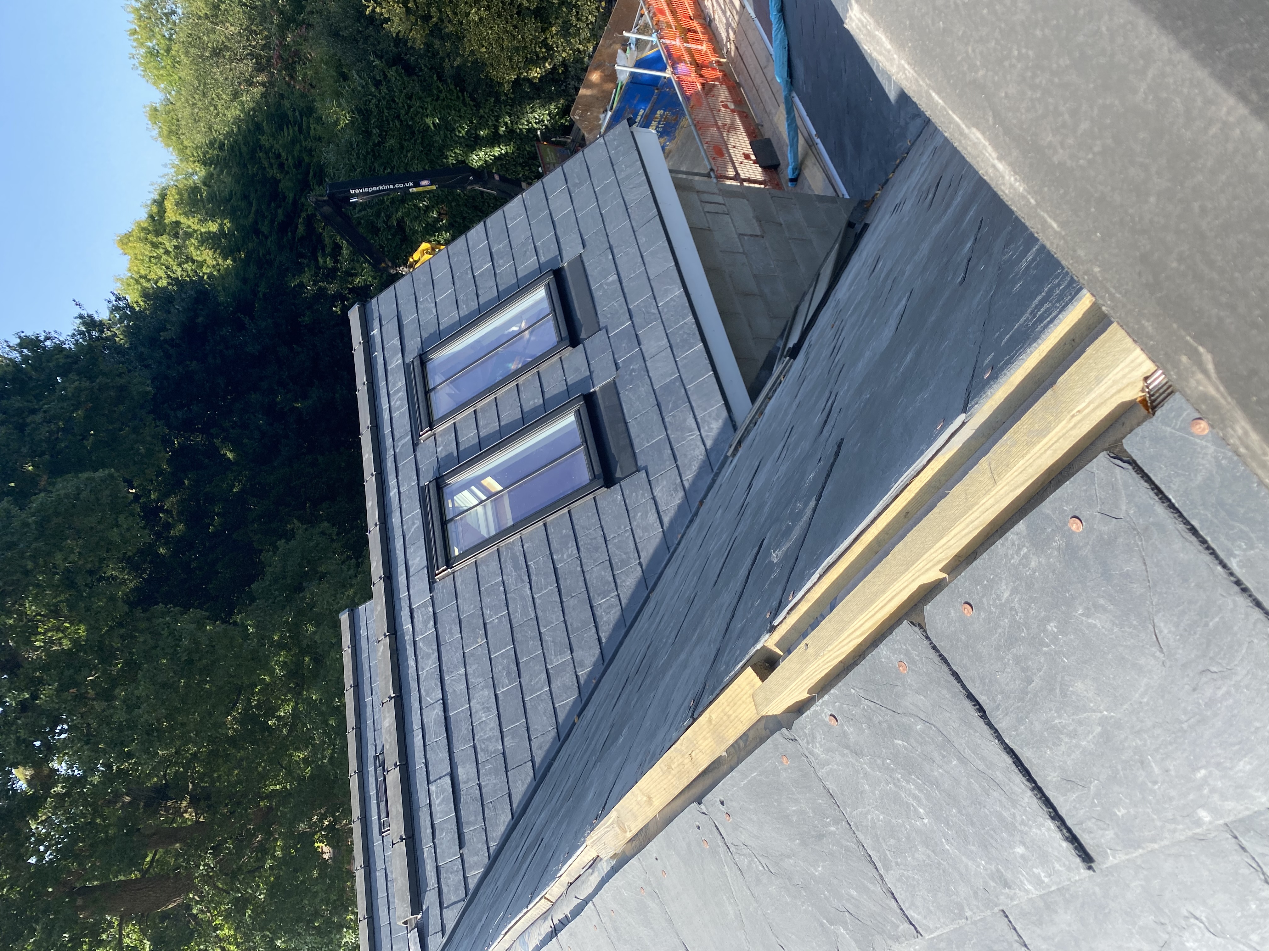 Pitched roof re-covered in grey slate above a red brick house