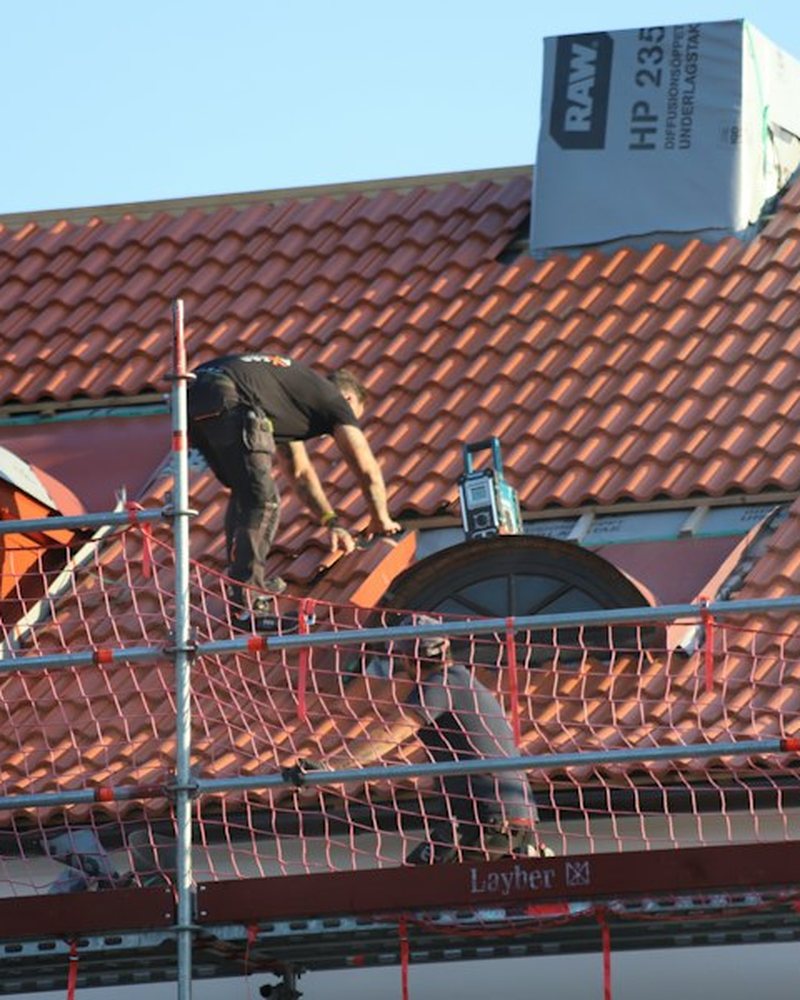 Roofer laying clay tiles on a scaffolded pitched roof