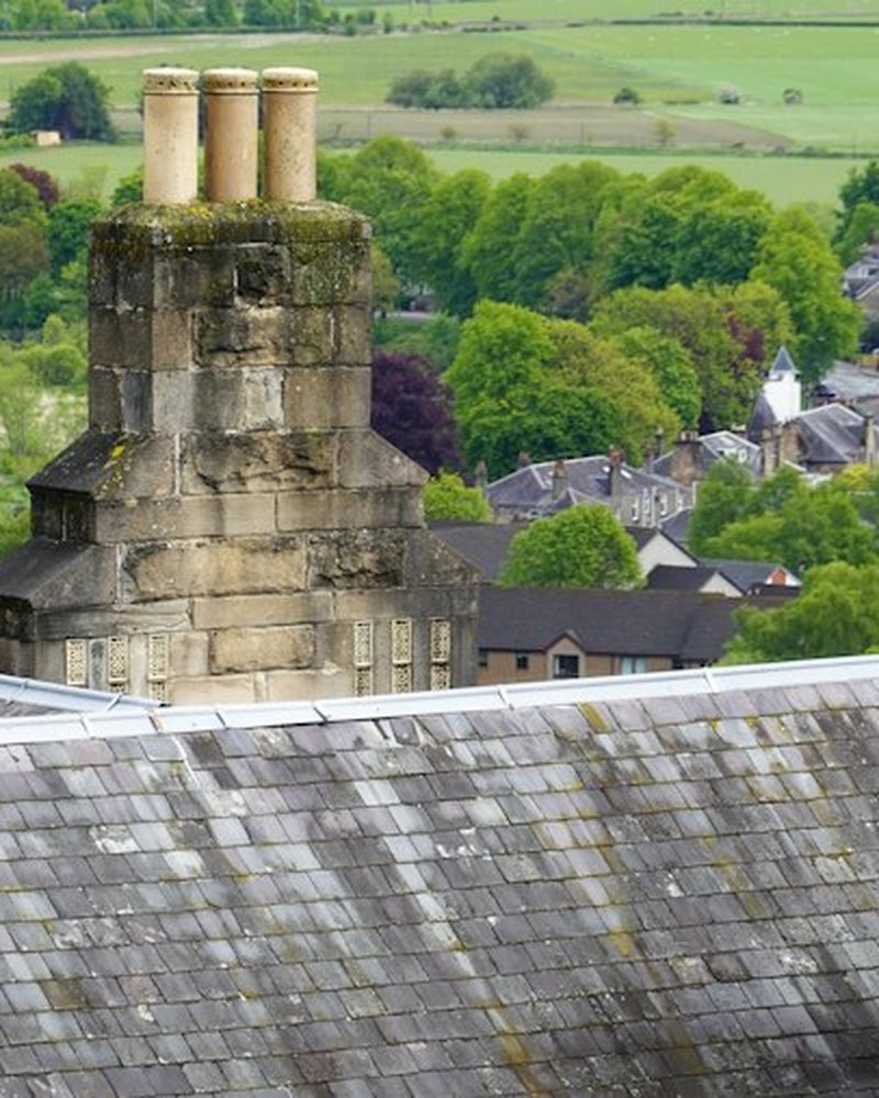 Stone chimney stacks on a slate roof above green fields