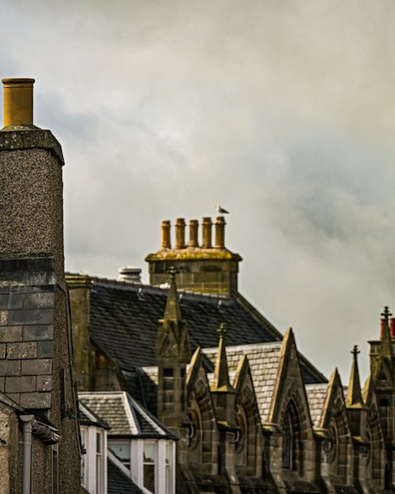 Stone and slate rooflines with chimneys against a cloudy sky