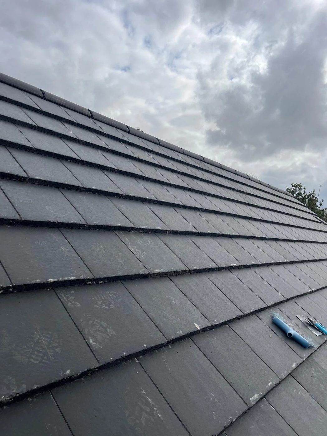 Dark tiled roof slope with roofing tools resting on the battens