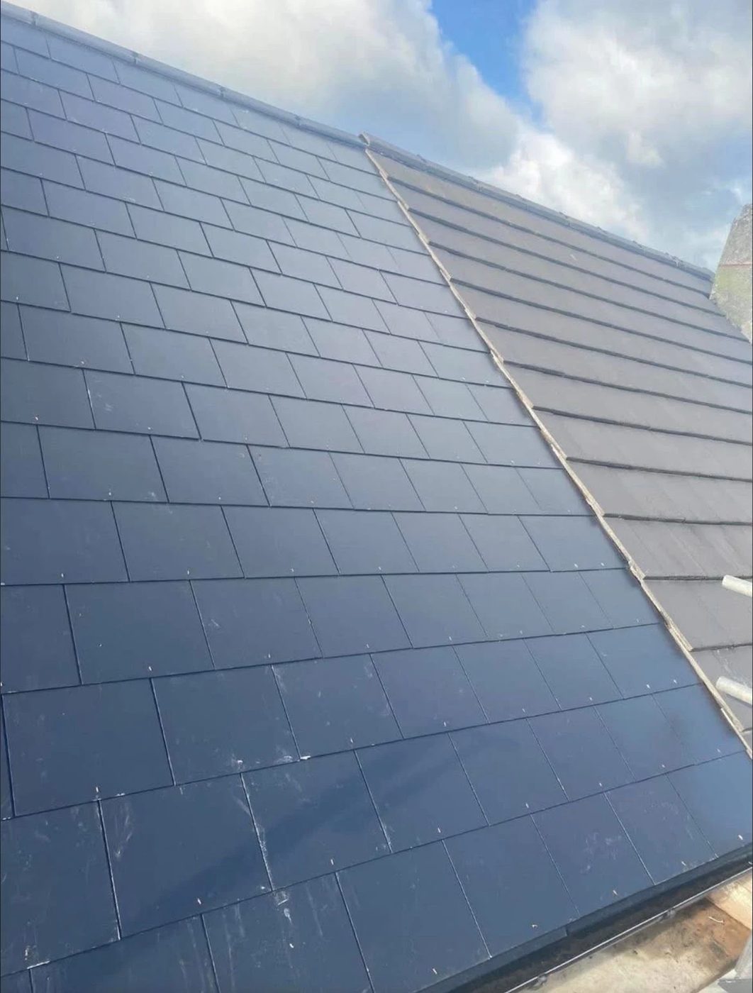 Wide dark tiled roof slope finished neatly under a blue sky