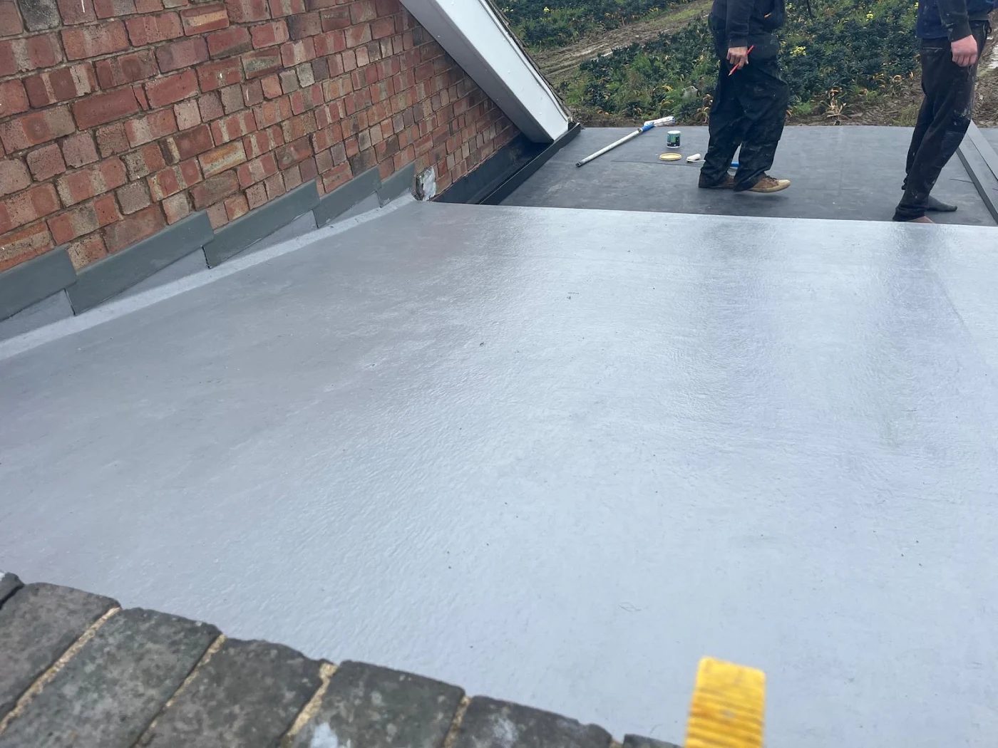 Flat roof membrane finished tidily at a brick parapet, with two roofers behind