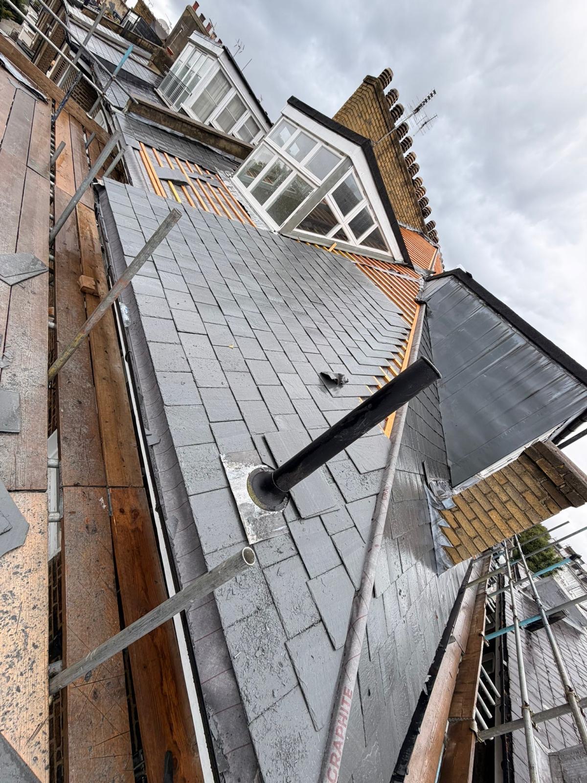Pitched roof covered in new grey slates with lead flashing running up to a brick chimney