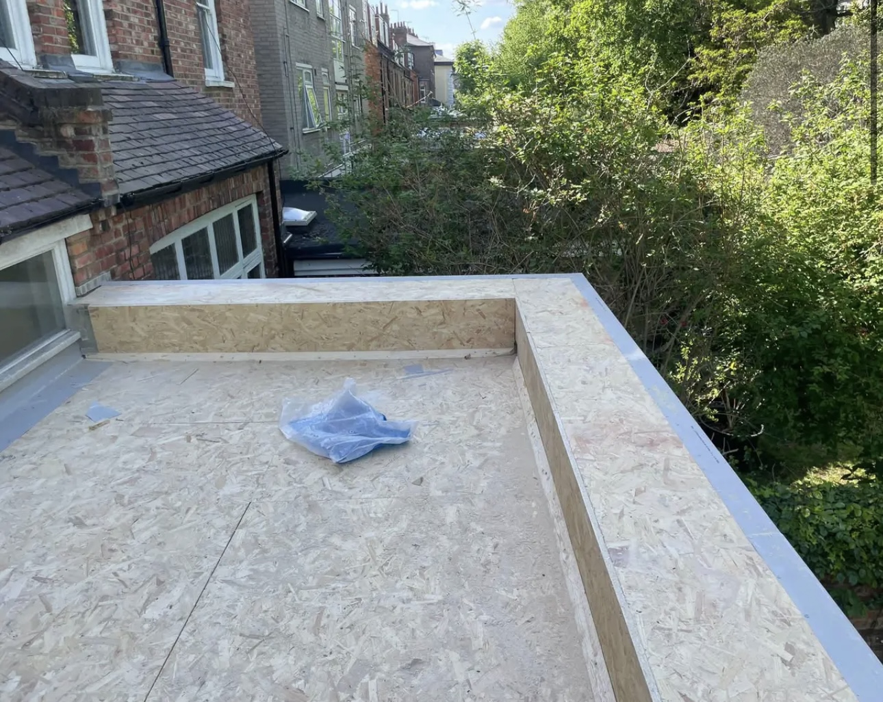 New timber decking laid across a flat roof on the back of a house, with a raised edge upstand all the way round