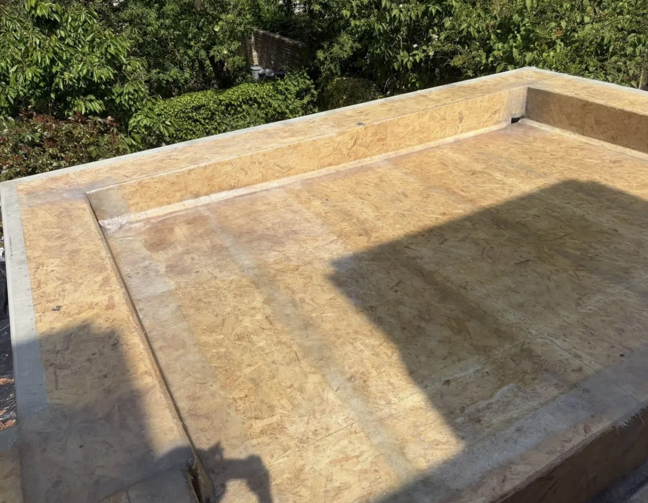 Close view of a freshly boarded flat roof deck with the upstand fitted along the parapet