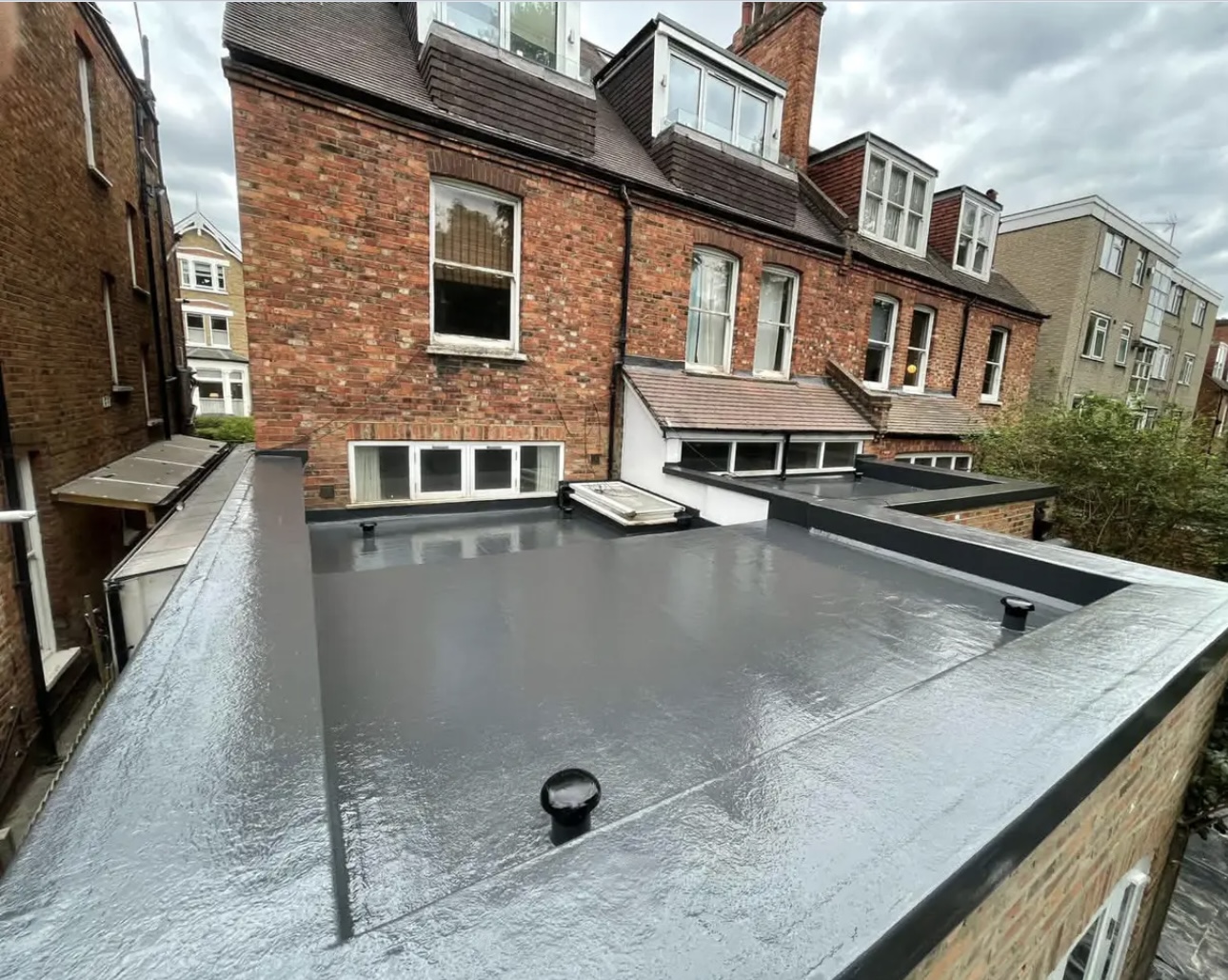 Finished grey flat roof covering on the back of a brick terrace, with a vent pipe and a neat trimmed edge