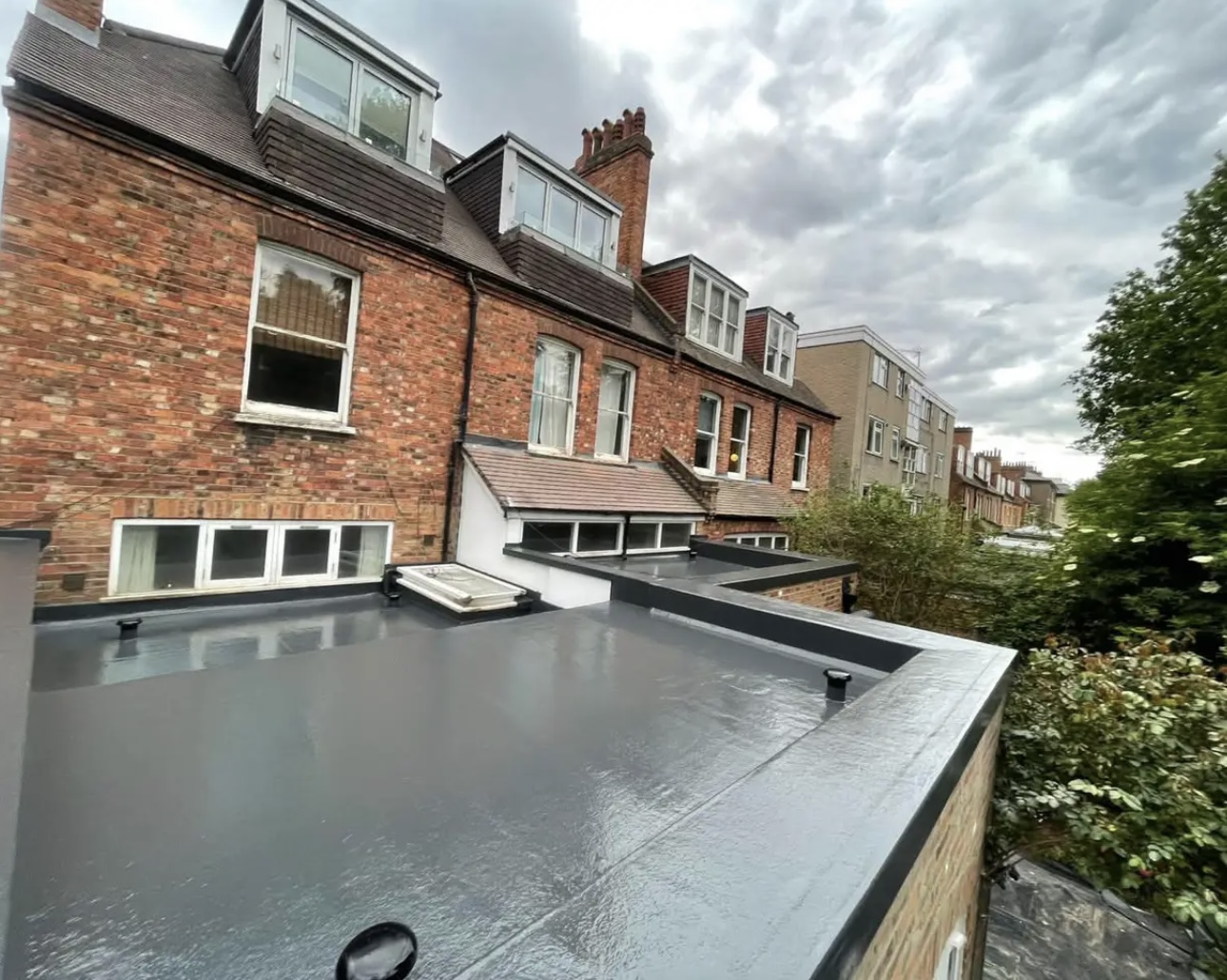 The same grey flat roof from the other end, with rooflights and the pitched slate roofs of the terrace behind