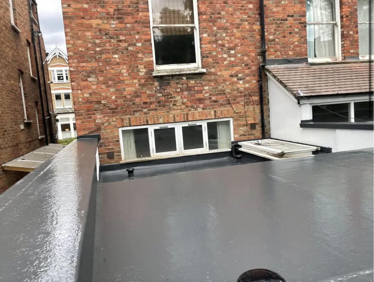 Completed grey flat roof over a rear extension, seen from the scaffold above the patio doors