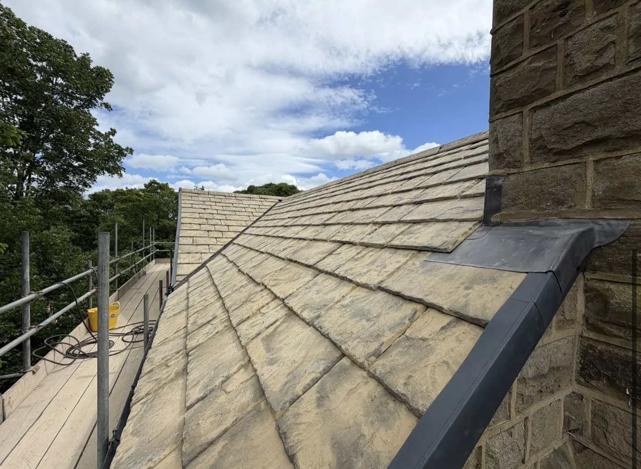 Grey slate roof slope finished up to a stone chimney stack, with lead flashing dressed in at the join