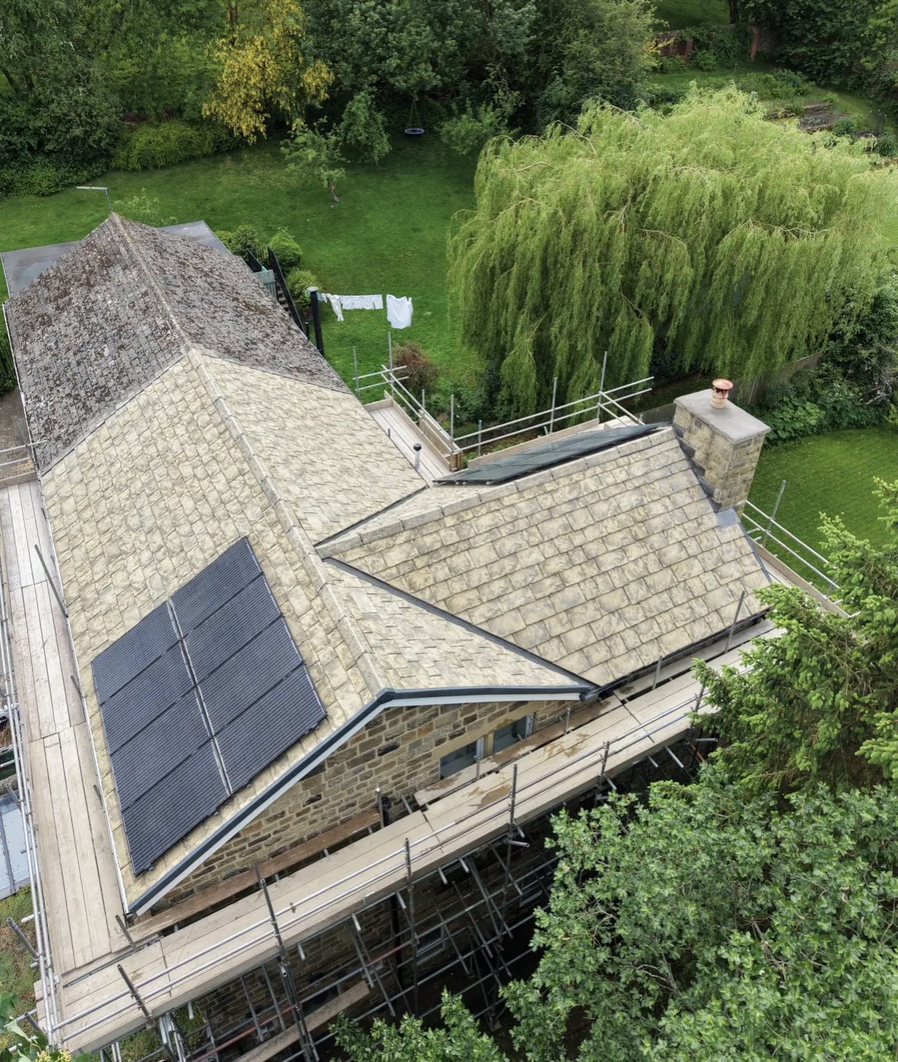 Stone-tiled roof photographed from above, solar panels on one slope and scaffolding round the house