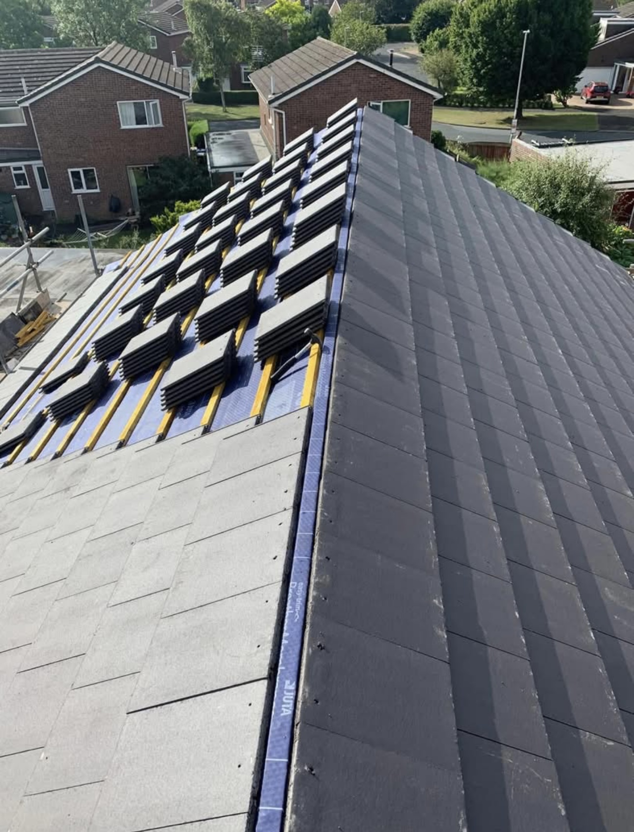 Dark grey tiles going on over the battens partway up a roof slope, houses and a street beyond