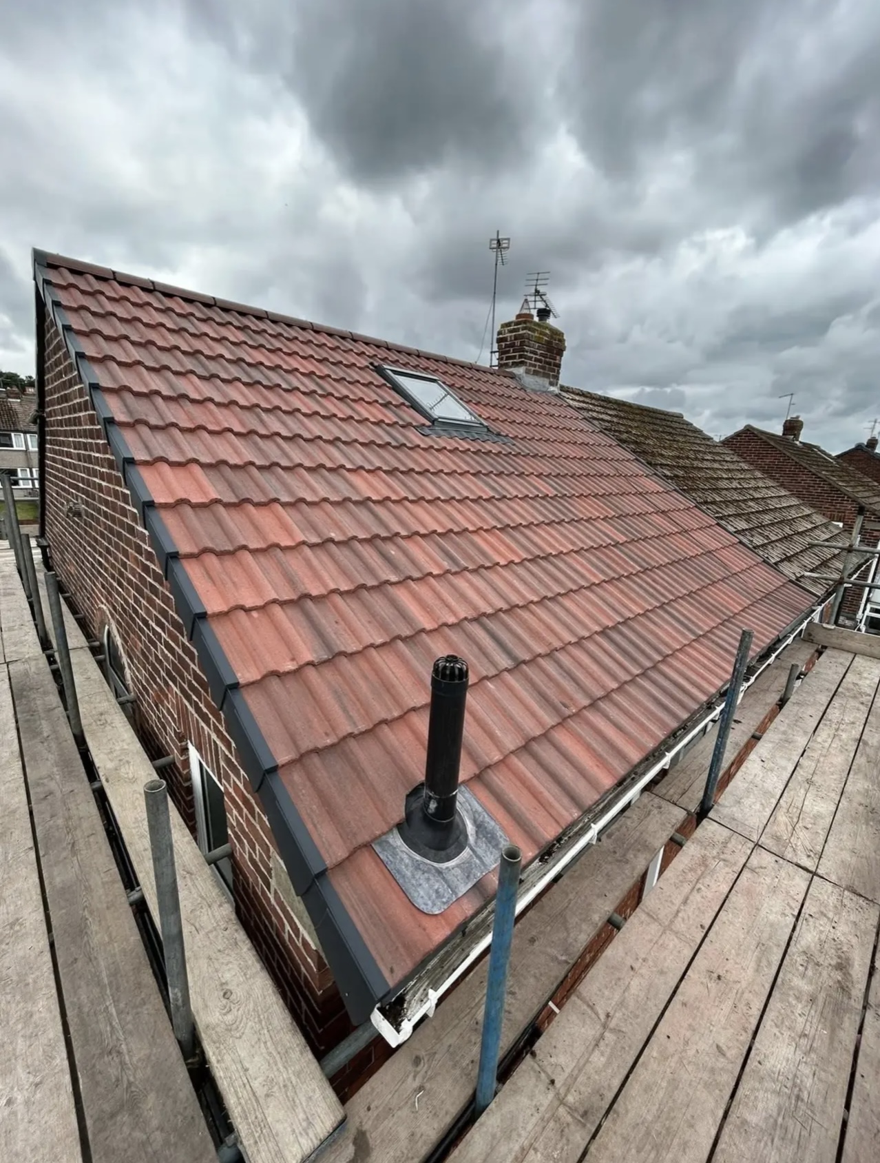 Red tiled roof slope with a new soil vent pipe fitted through it and scaffold boards along the eaves