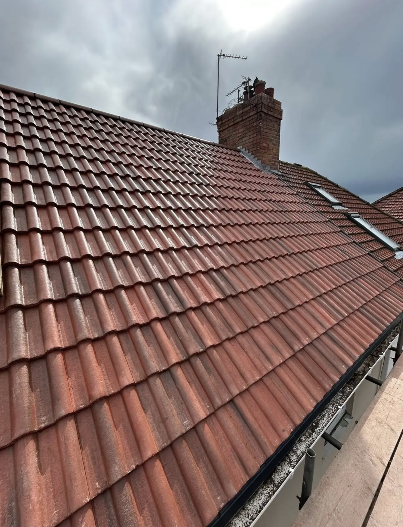 Red pantile roof slope running up to a brick chimney, with a rooflight set into the tiles
