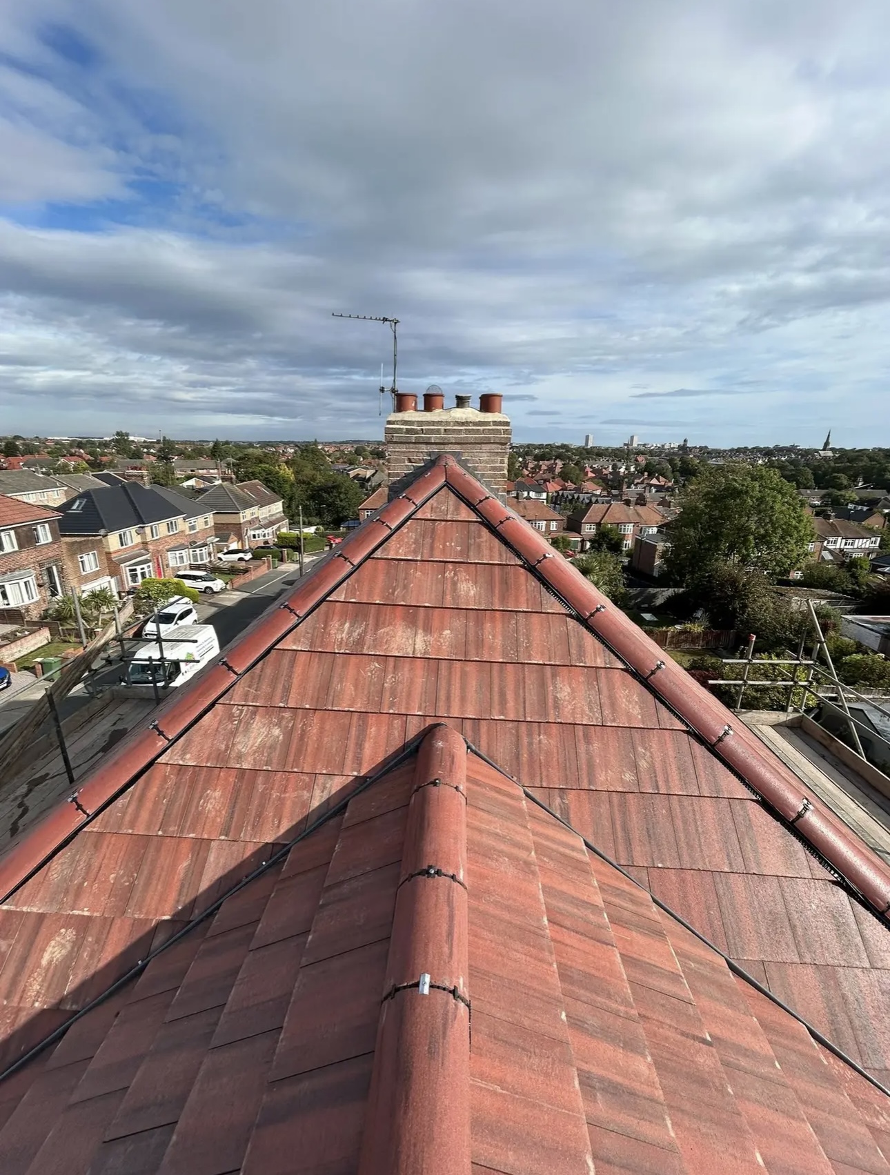 Red tiled hipped roof finished off, chimney pots at the ridge and rooftops stretching away behind