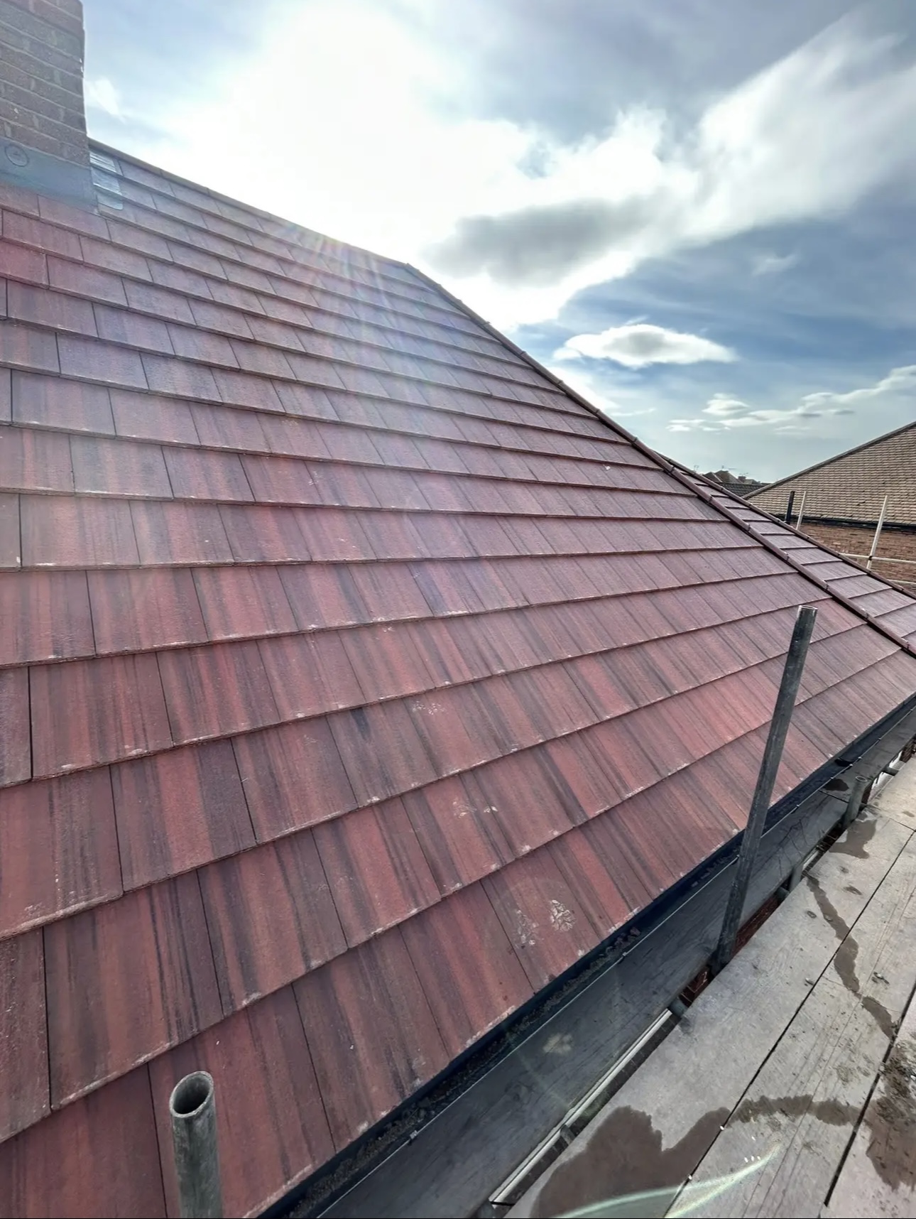 Long red tiled slope on a sunny day, ridge and hip tiles bedded in and scaffold along the bottom