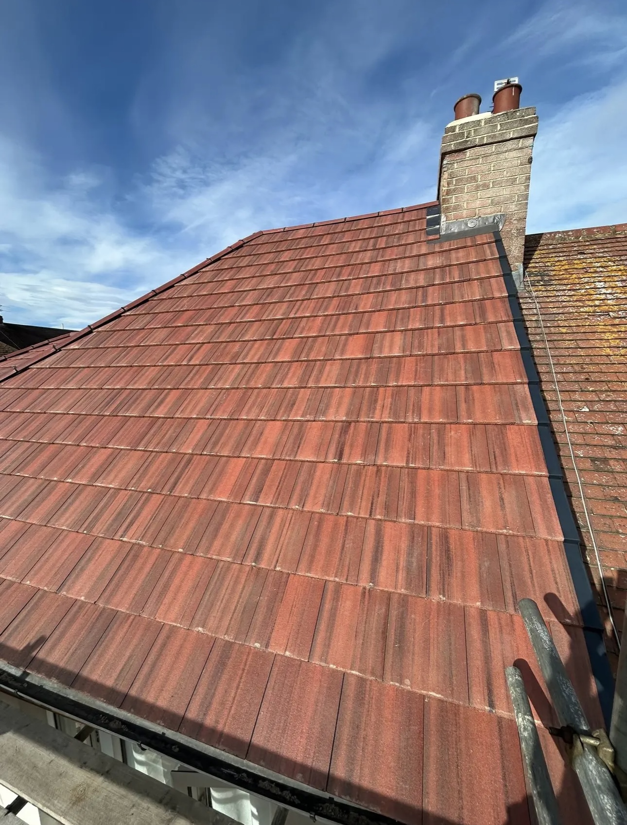 Red tiled roof slope against a blue sky, running up to a brick chimney stack