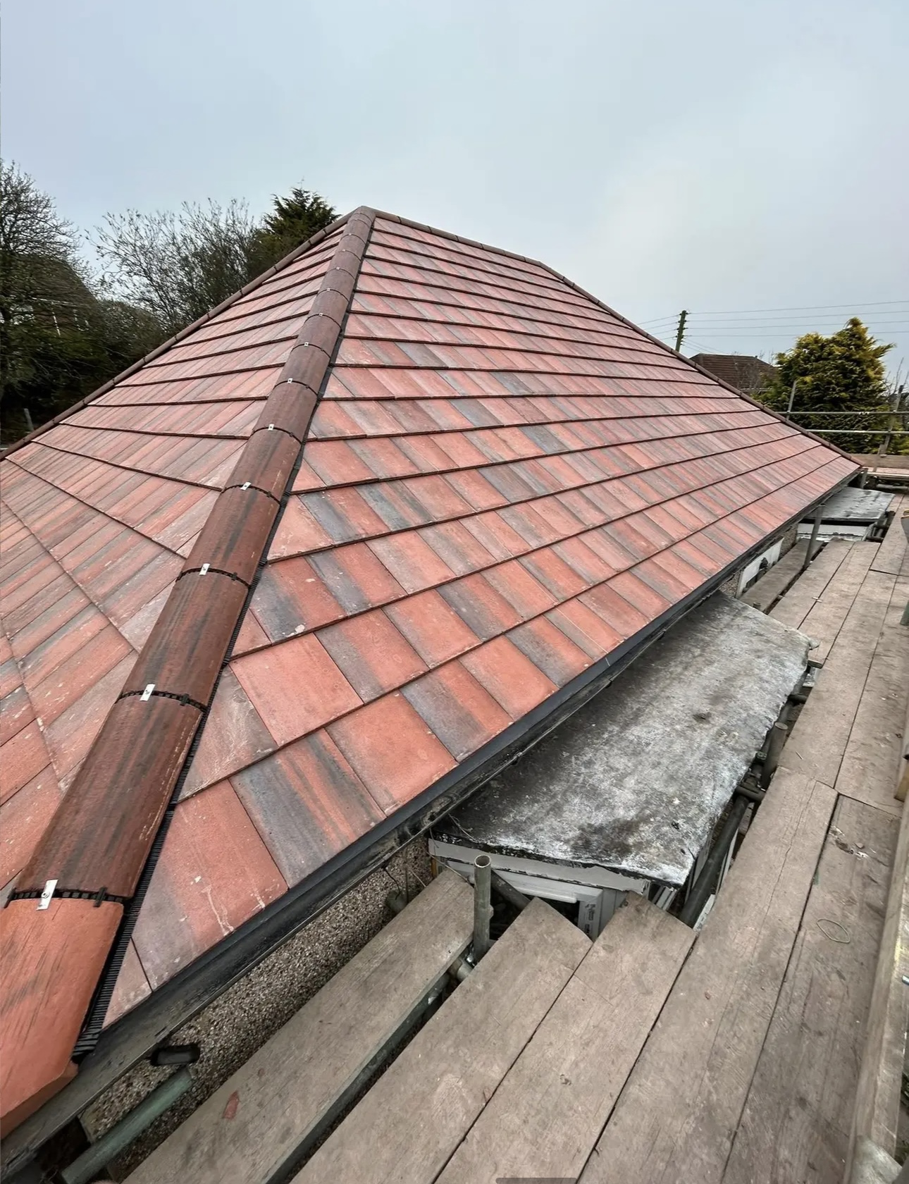 Red tiled hipped roof with the hip tiles run in a straight line, scaffold boards along the edge