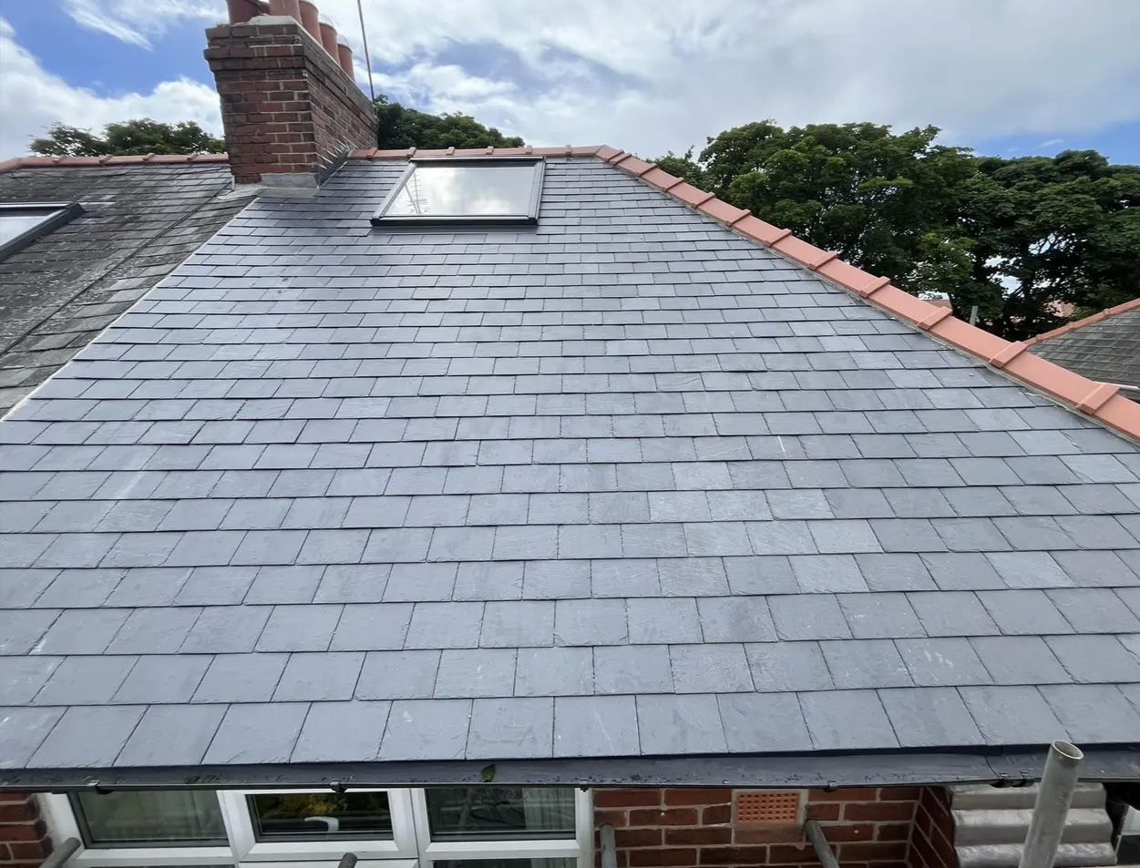 Grey slate roof with rooflights on a brick house, seen from the scaffold