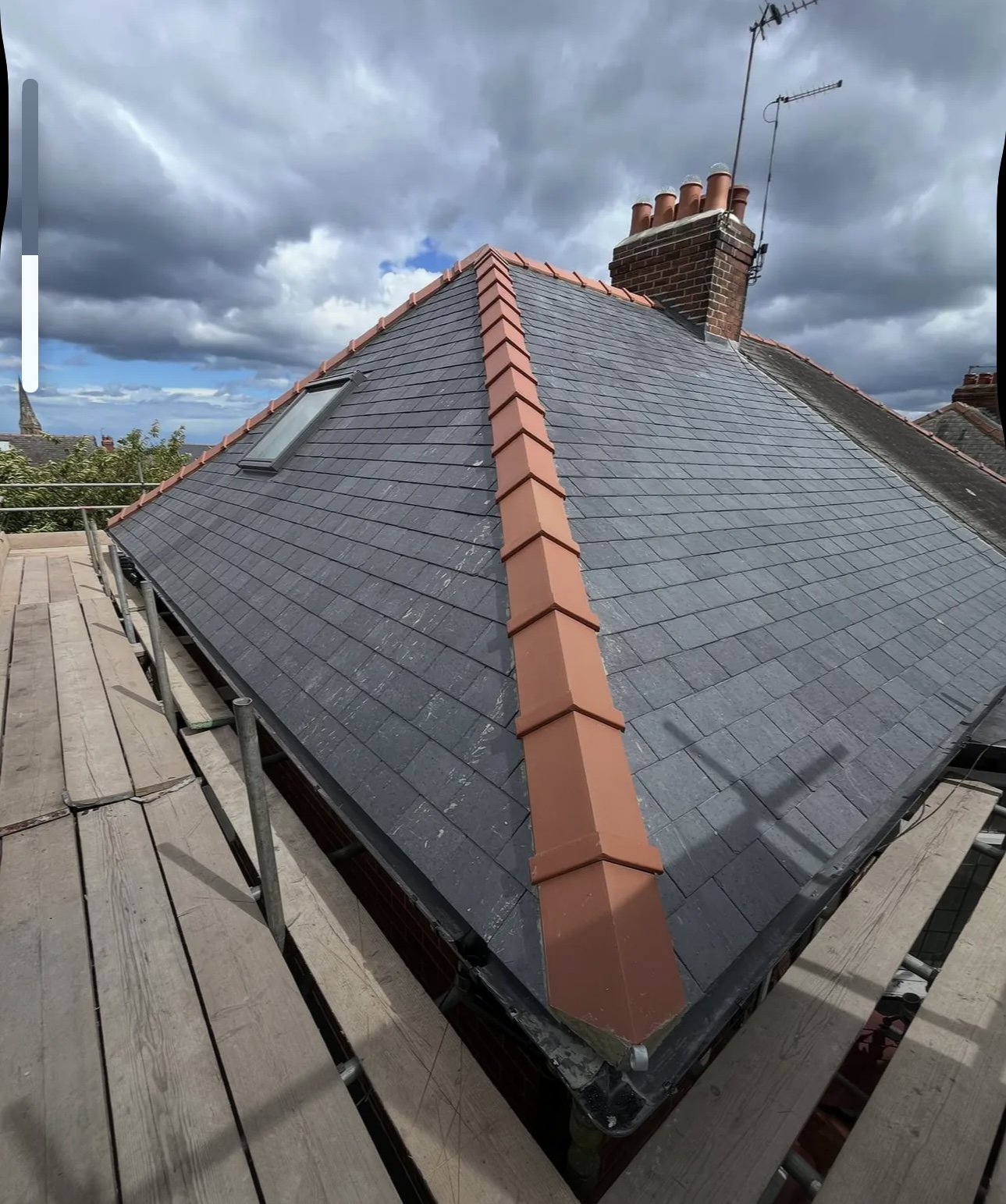 Grey slate hipped roof with red hip tiles, scaffold boards running along the gutter line