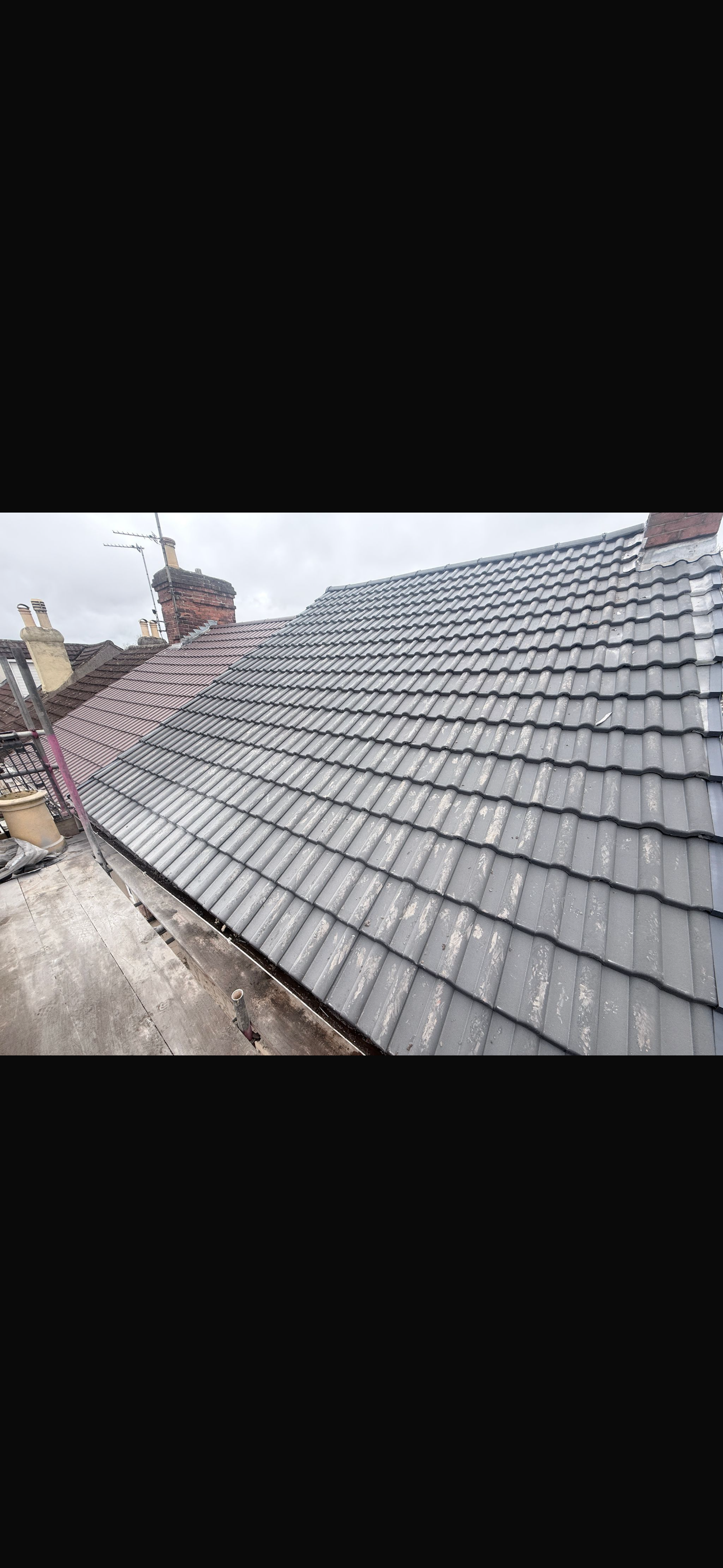 Close view across a grey tiled pitched roof beside a chimney