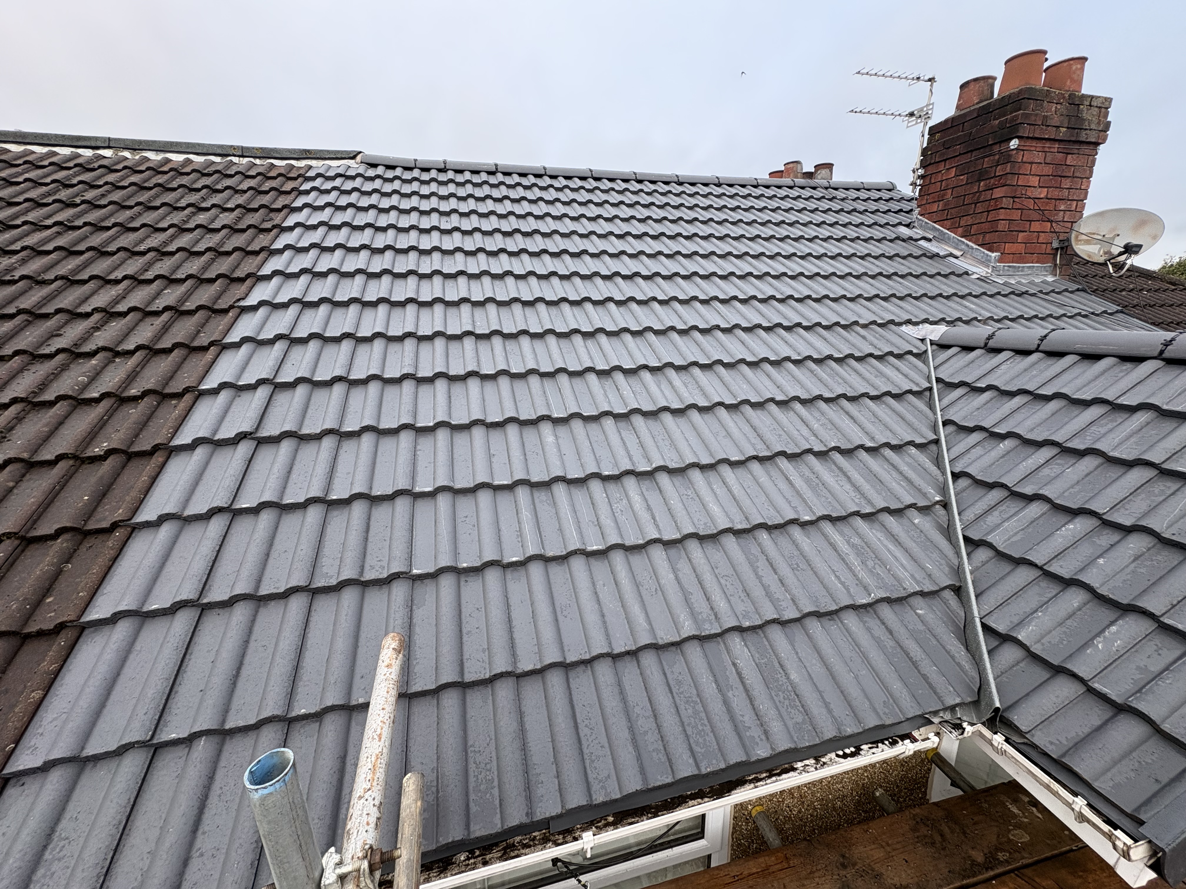Fresh grey roof tiles laid across a pitched roof beside scaffolding