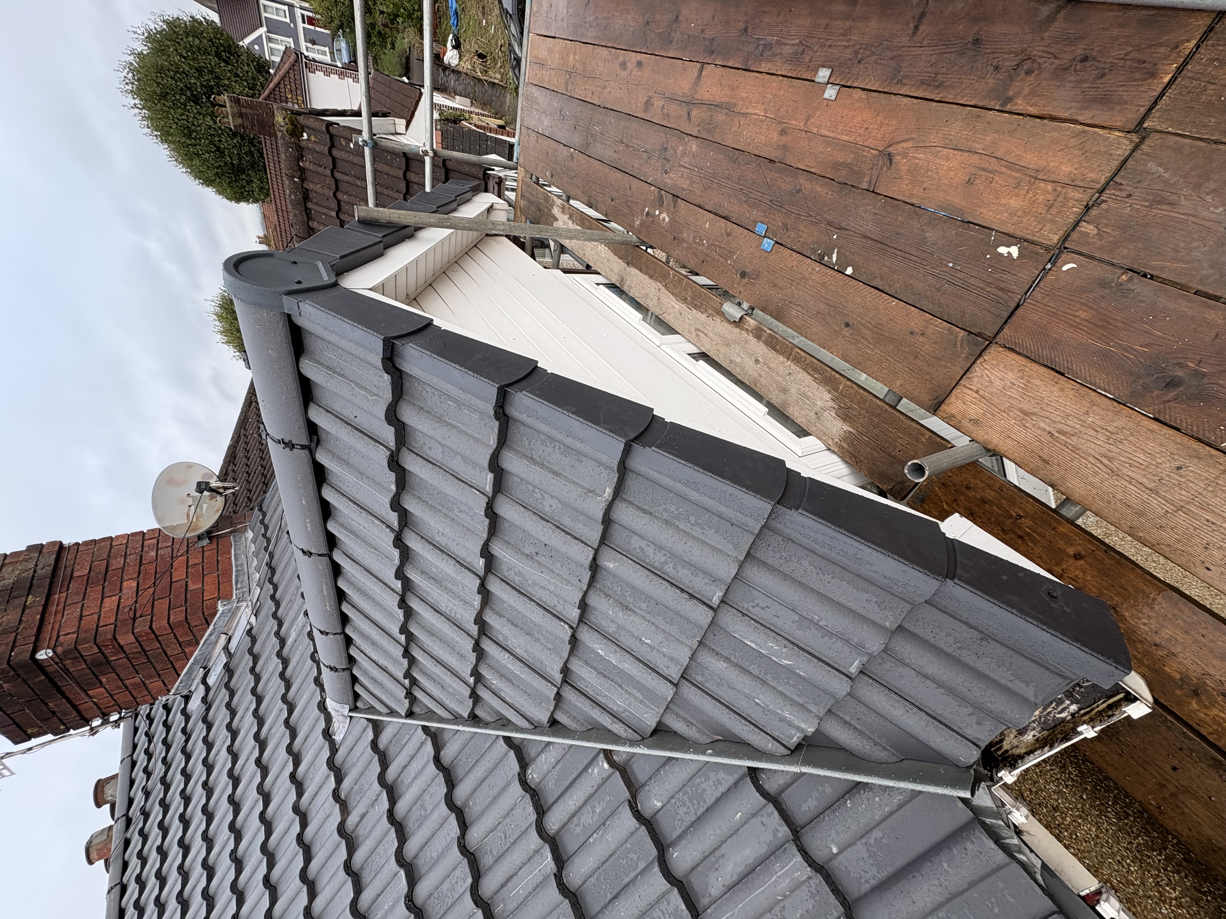 Grey tiled roof edge with a white gutter and brick wall alongside