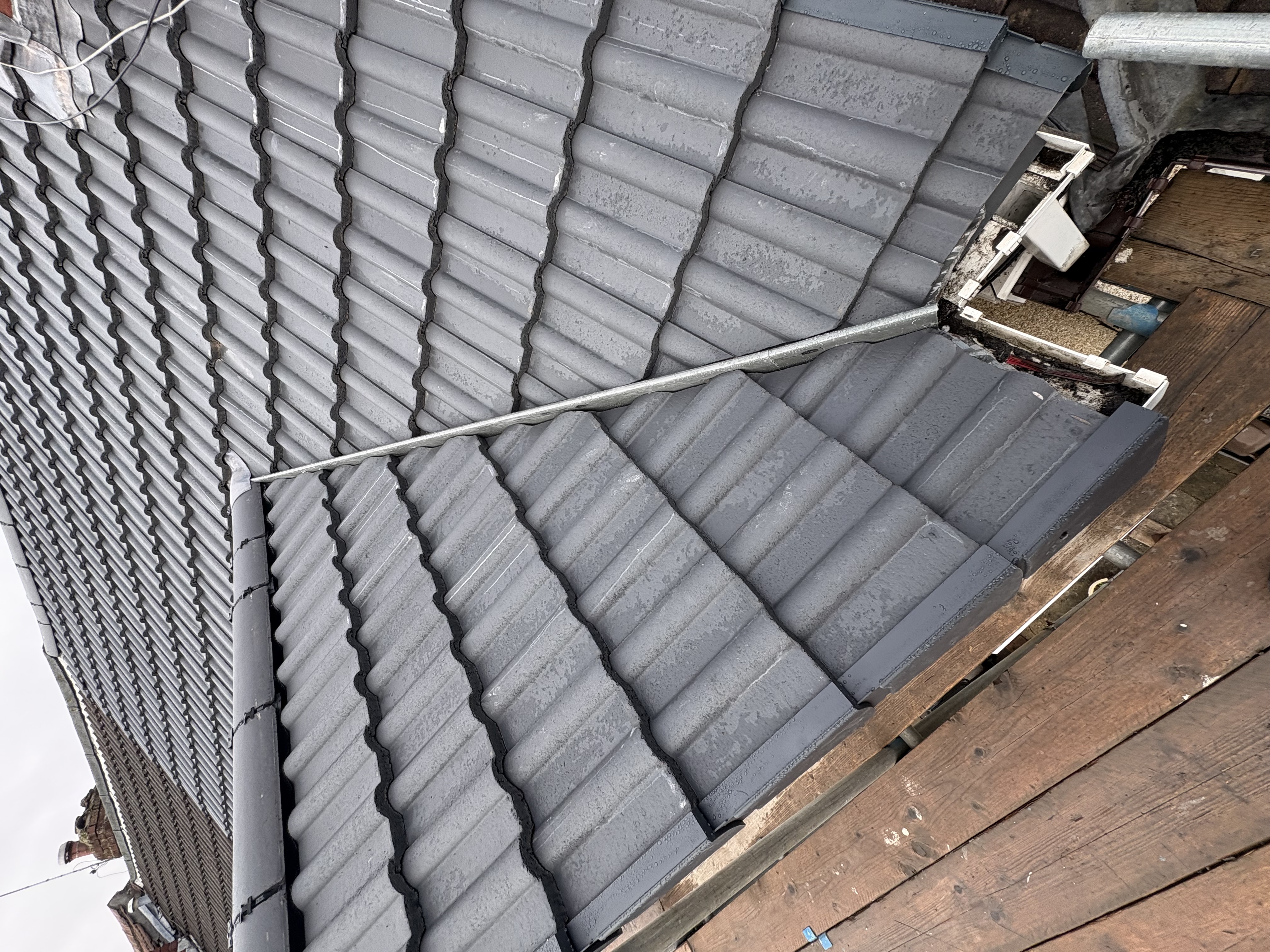 Grey roof tiles and guttering viewed from above near a brick chimney
