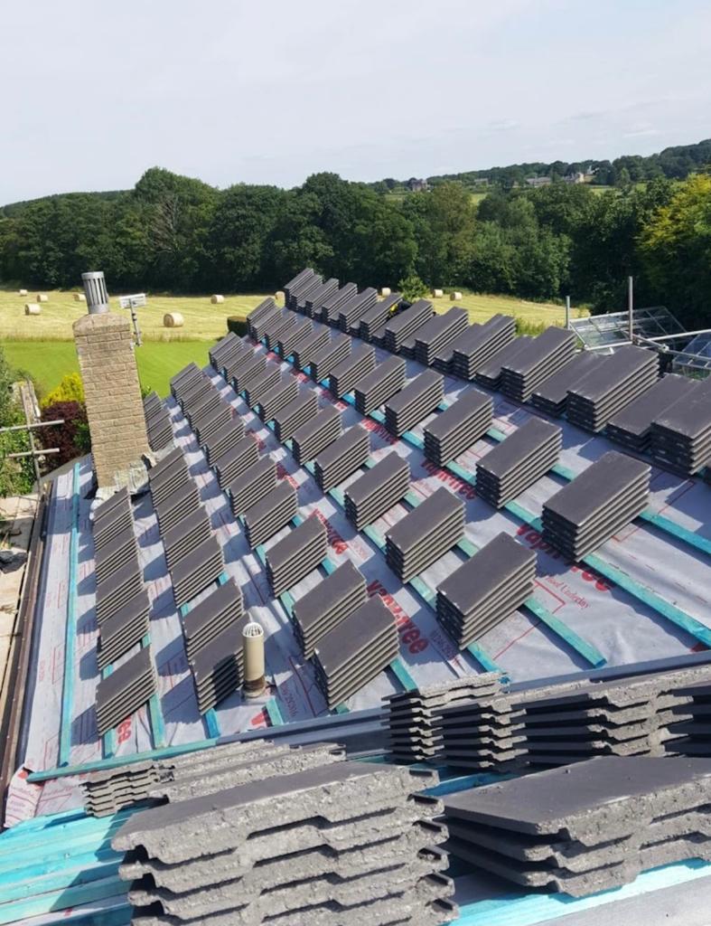 Rows of new grey roof tiles being laid over blue membrane
