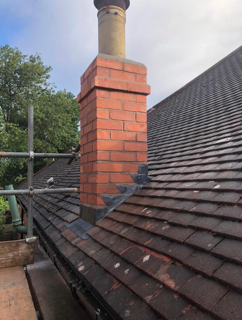 Rebuilt red brick chimney on a dark tiled roof