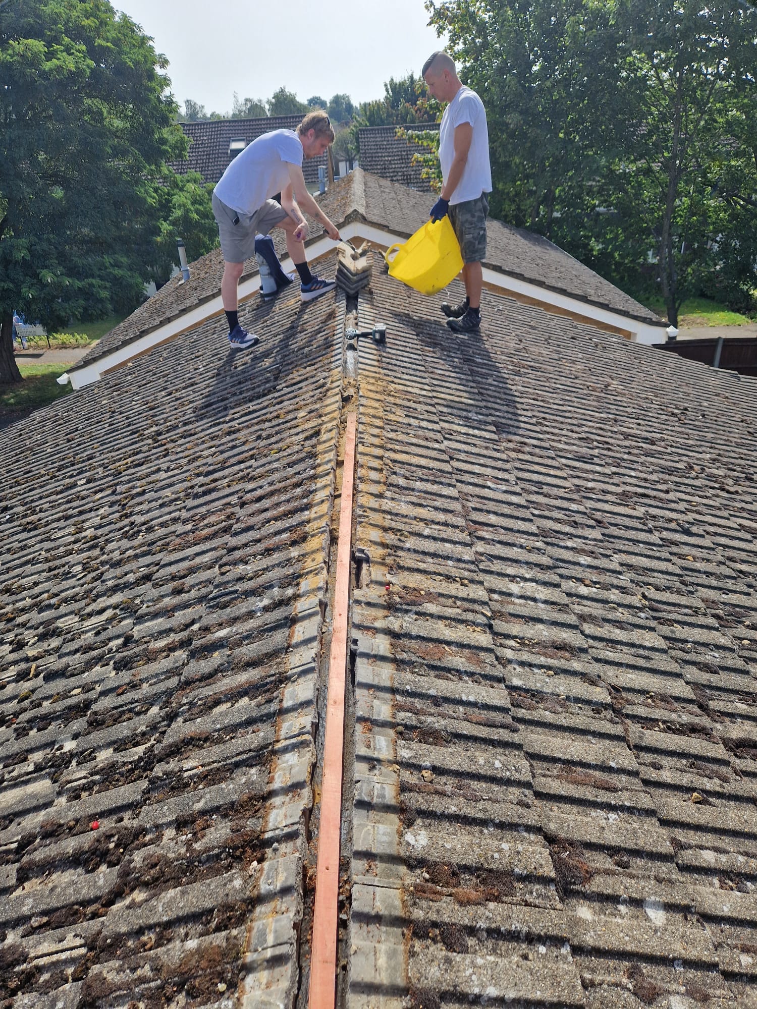 Roofers renewing the ridge of a weathered tiled roof