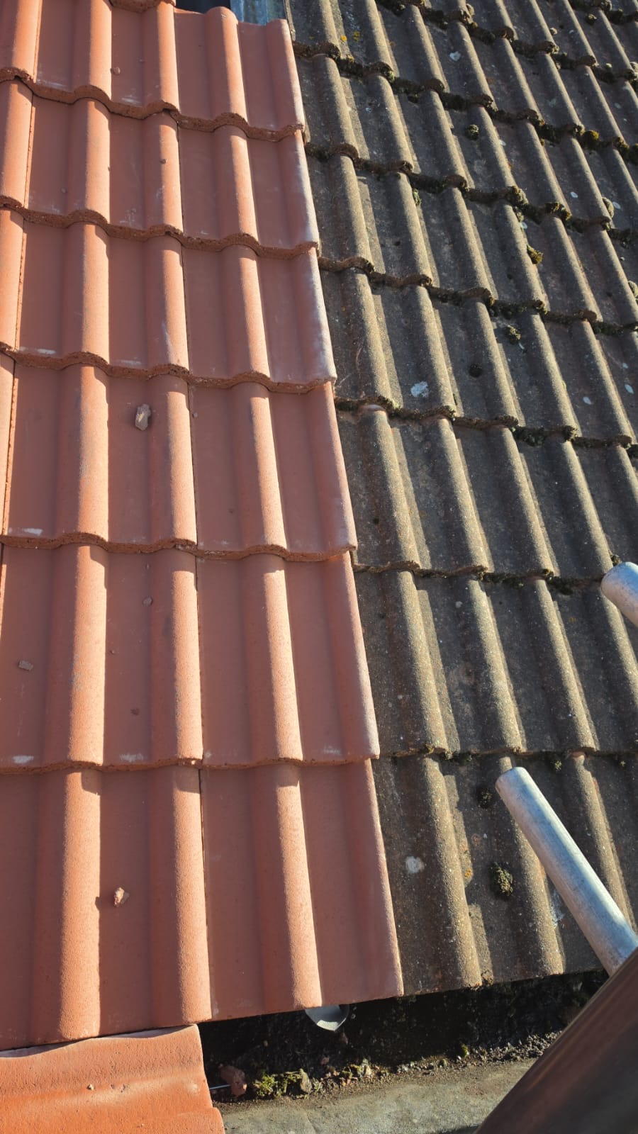 New red interlocking tiles laid beside older grey concrete tiles on a pitched roof