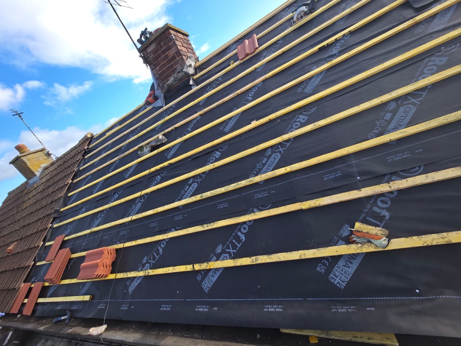 Pitched roof stripped back to breathable membrane and new timber battens, chimney in the background