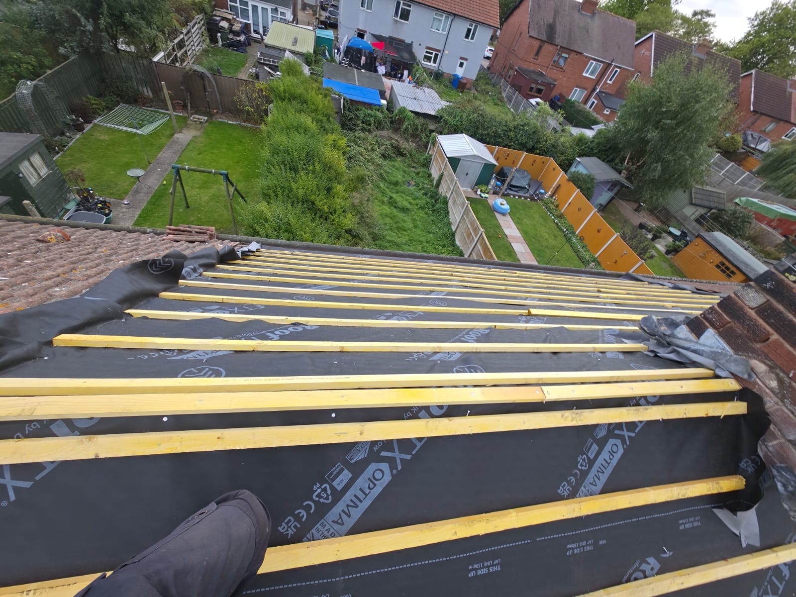 Freshly battened roof over membrane, looking down onto back gardens of a row of houses