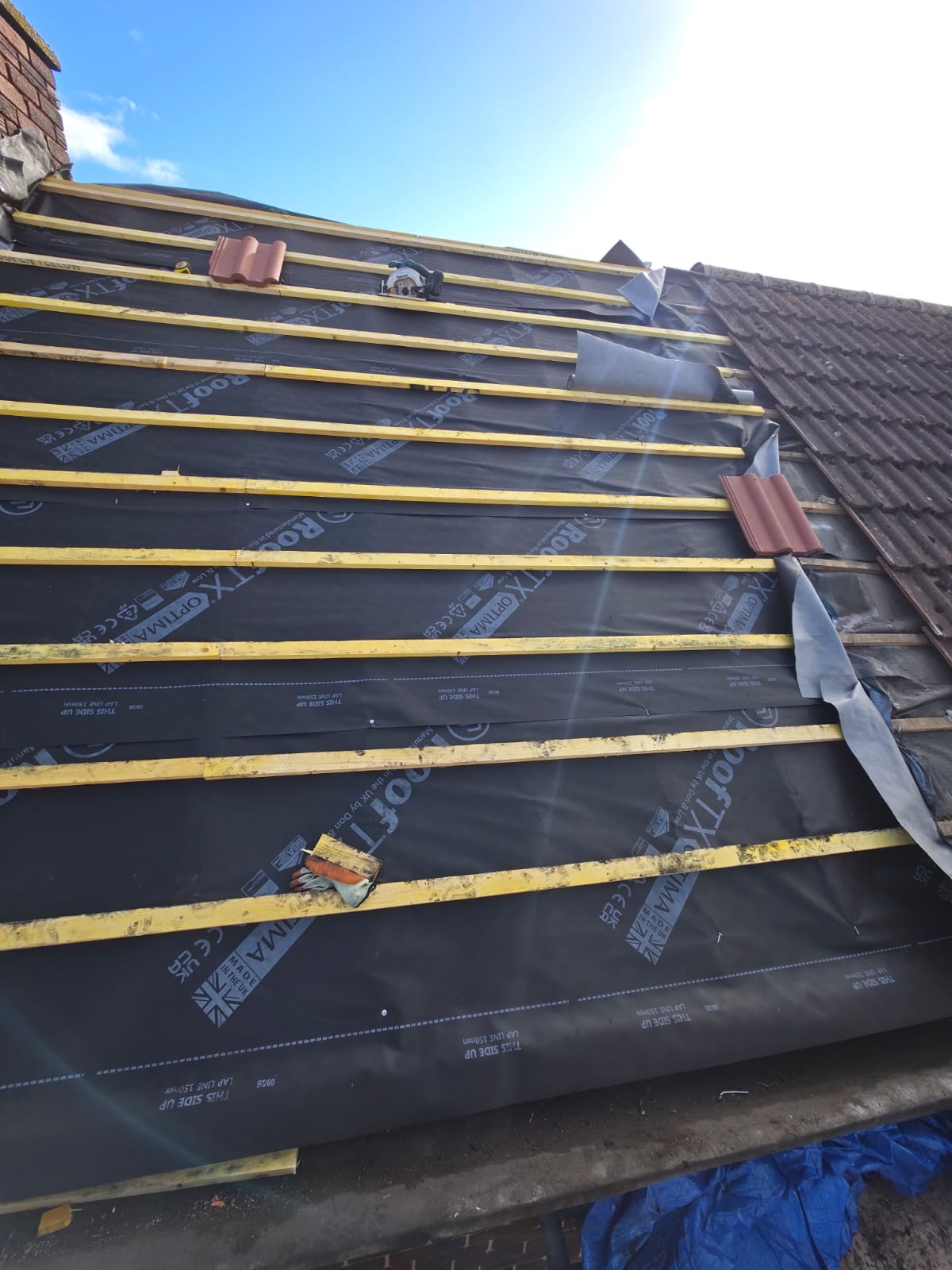 Roof slope covered in new membrane with evenly spaced battens under a blue sky