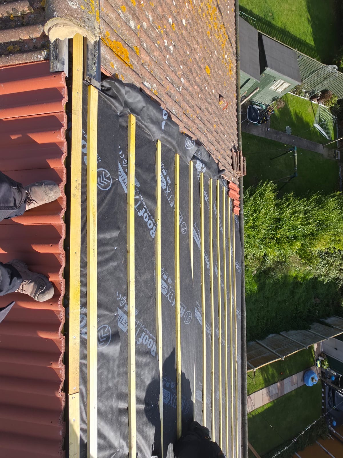 Red tiles and new battens running along the edge of a roof above a garden